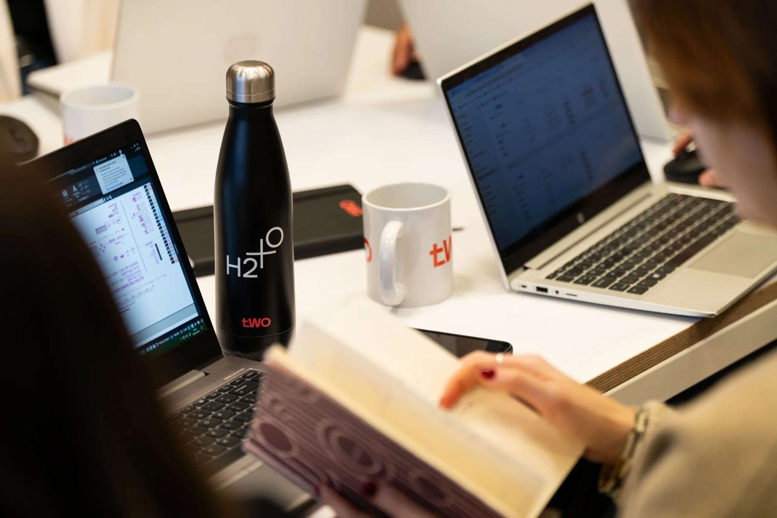 Meeting with Two employees with Two mugs, water bottles and notebooks displayed.