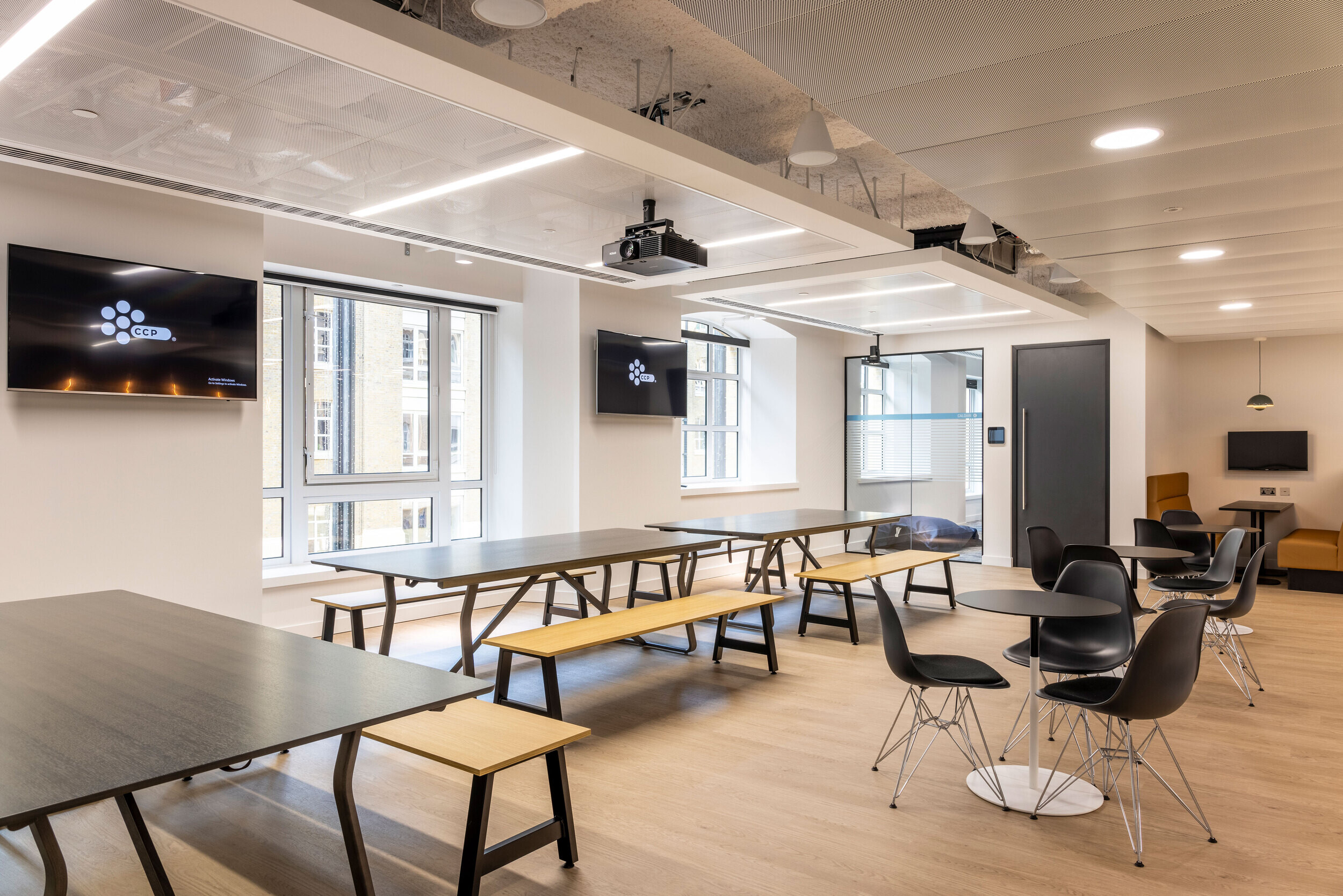 Collaborative communal area in CCP Games' office designed by Two, with long wooden benches and tables, modern lighting, and open-plan design.