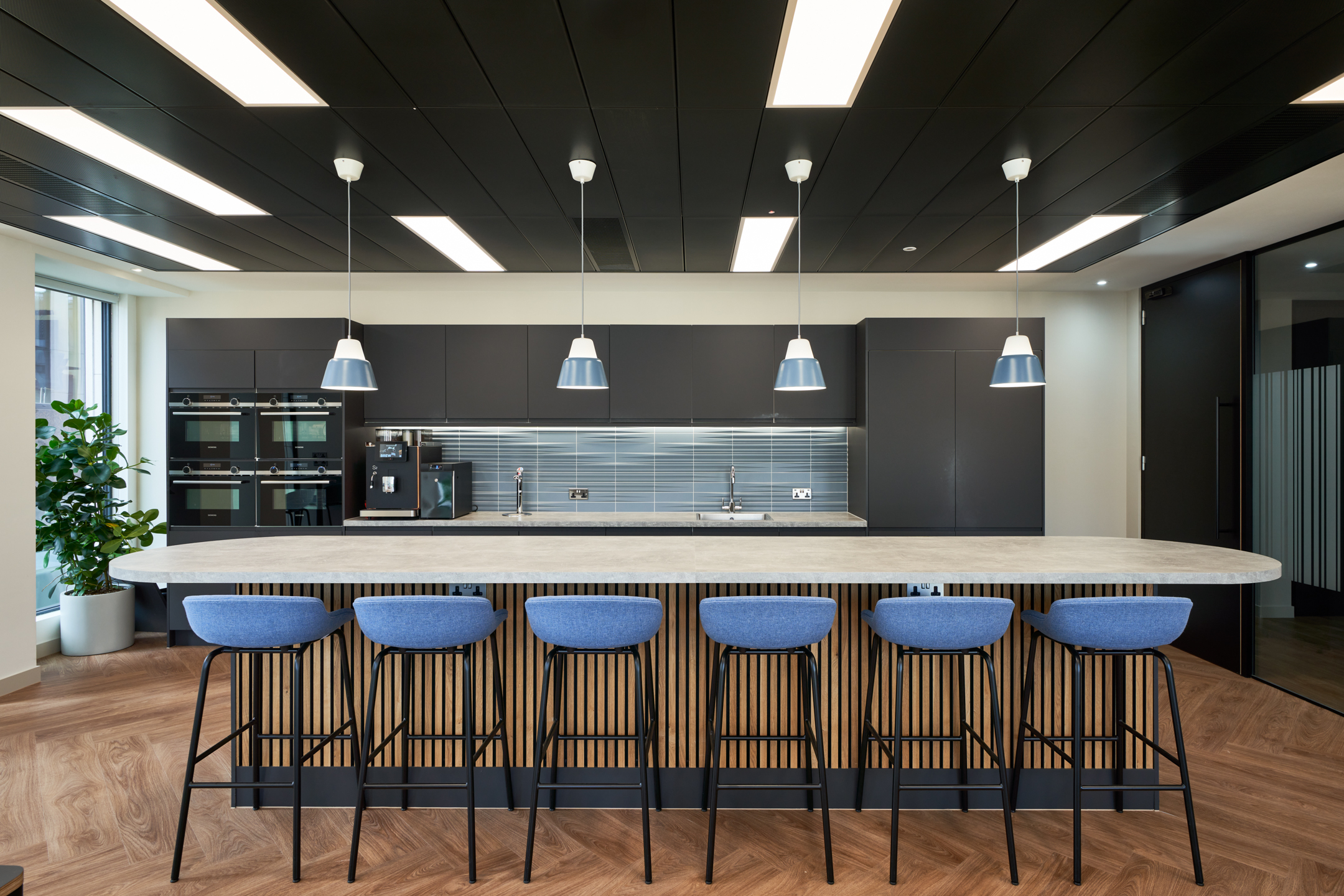 A large teapoint with pendant lighting and kitchen amenities behind.