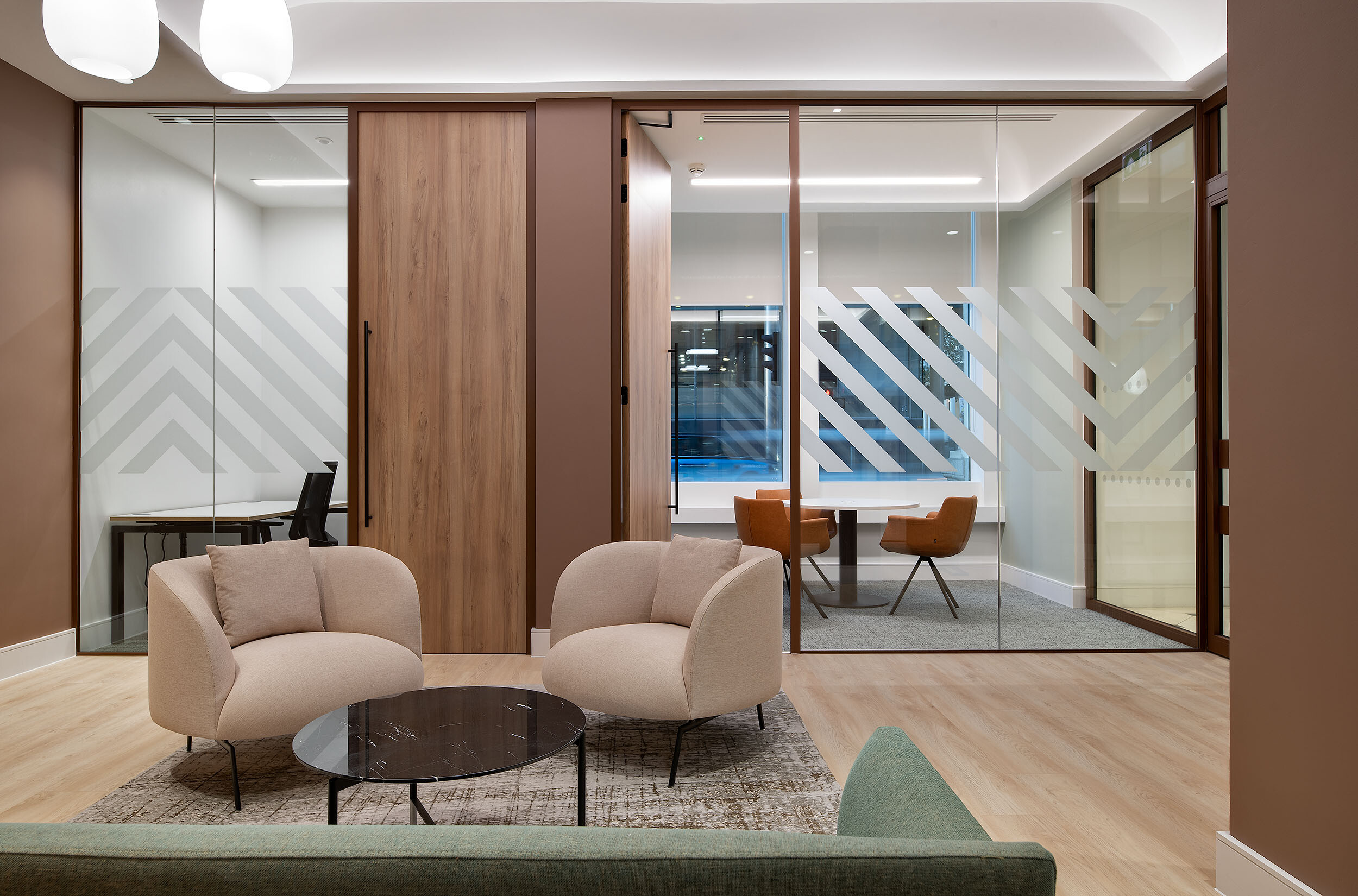 A refined meeting and lounge area at 123 Pall Mall, designed by Two, featuring bespoke manifestation on glass partitions, comfortable seating, and a blend of wood and neutral tones for a contemporary office aesthetic.