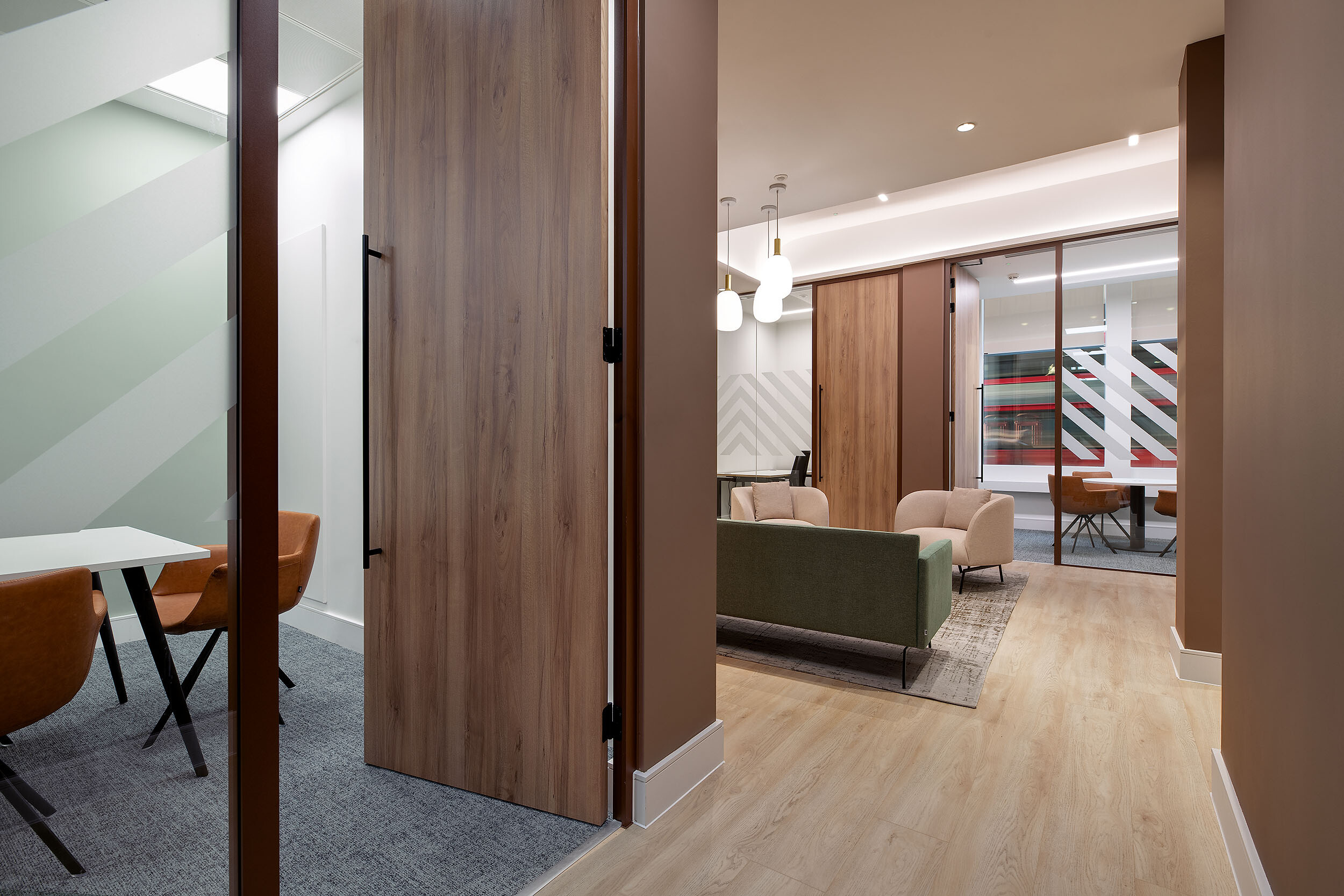 A corridor view at 123 Pall Mall, designed by Two, featuring wood-panelled doors, glass partitions, and a glimpse into the office’s lounge and meeting spaces, blending functionality with modern design.