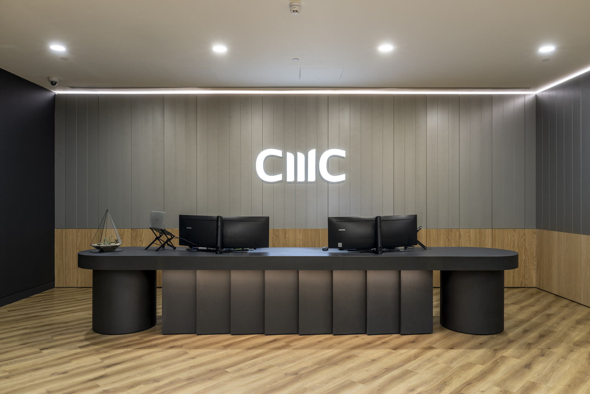 The sleek reception desk at CMC Markets' London HQ, designed by Two, features wood panelling, integrated lighting, and modern finishes.