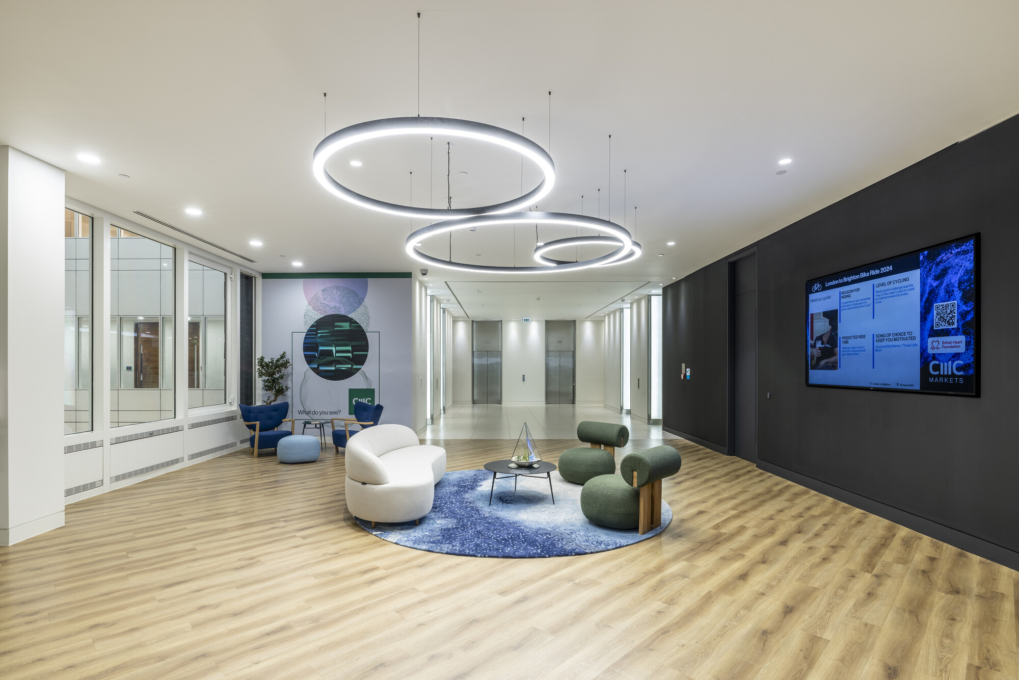 Modern breakout area at CMC Markets' HQ designed by Two, featuring circular LED lighting, contemporary seating, and wood-effect flooring