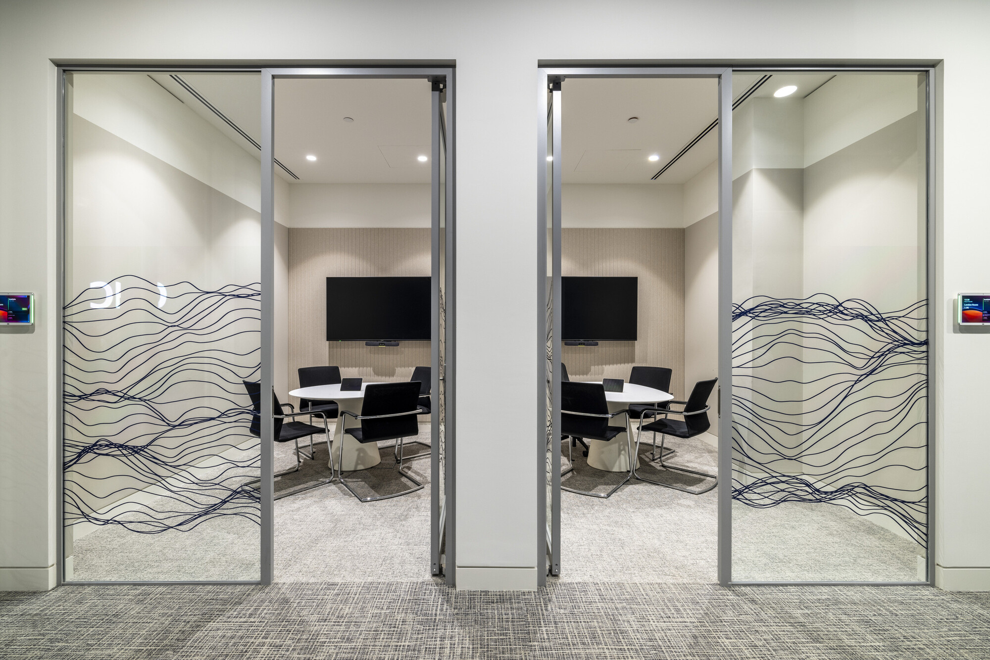 Meeting rooms at CMC Markets' HQ designed by Two, featuring glazing with wave patterns and integrated digital displays.