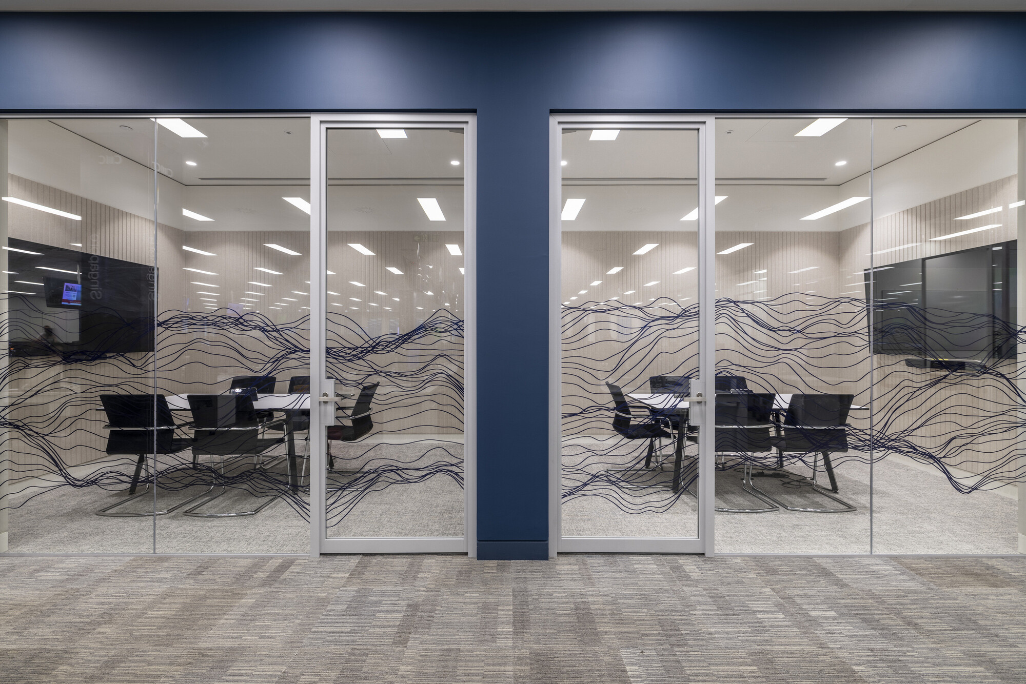 Dual meeting rooms at CMC Markets’ Whitechapel office designed by Two, featuring custom wave-patterned glazing for added privacy and aesthetic appeal.