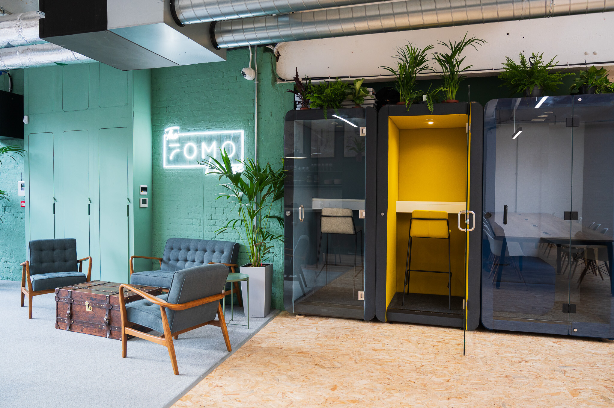 A cosy breakout area in the FOMO Rentals office by Two, featuring a vibrant yellow private phone booth and elegant seating options.