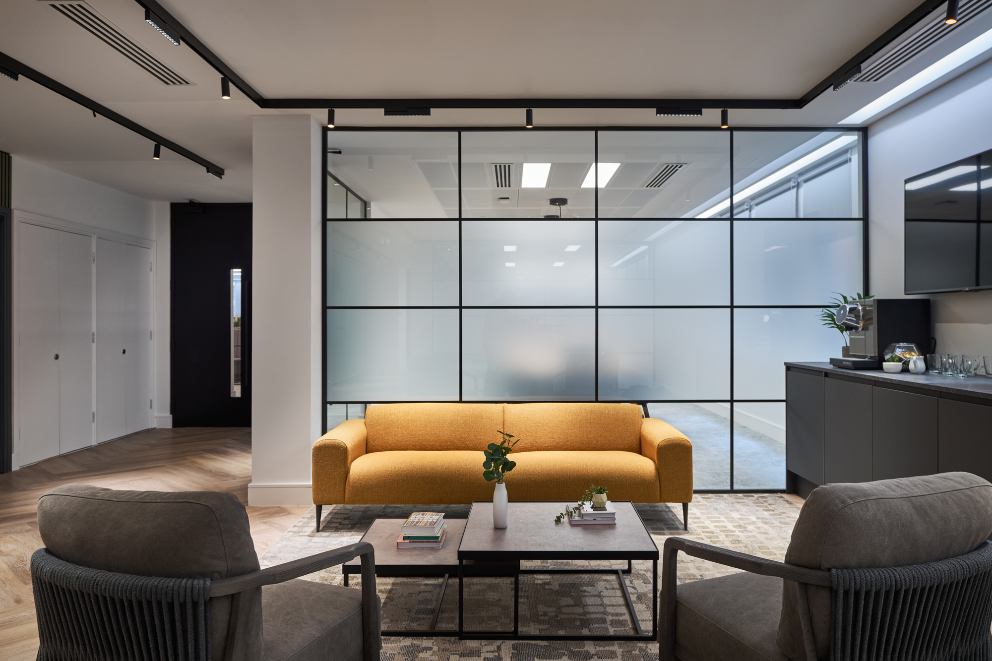 Gemserv's lounge area designed by Two, featuring a mustard sofa, grey armchairs, and frosted glazing for a modern yet inviting atmosphere.