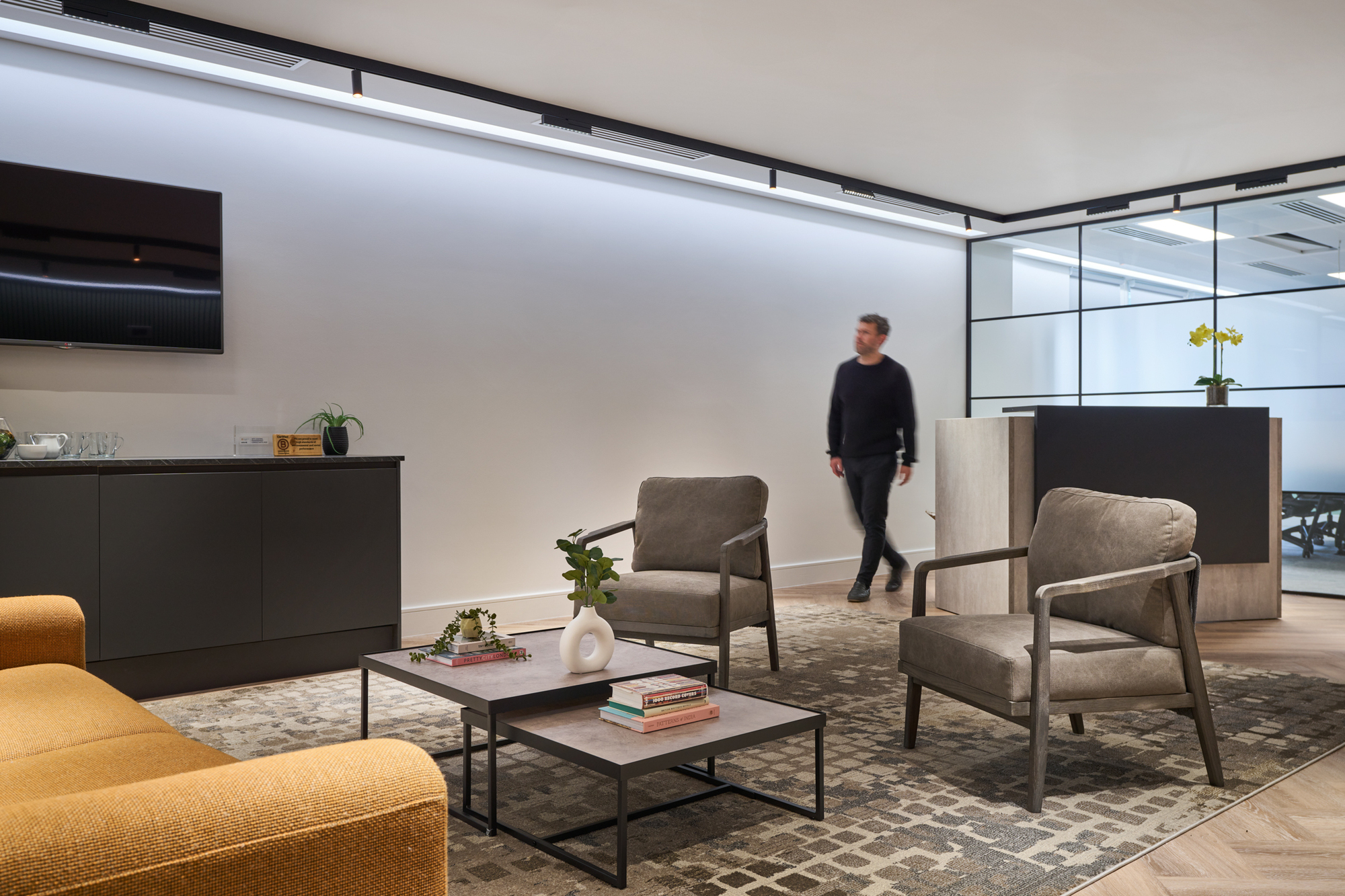 Sophisticated lounge in Gemserv’s workspace by Two, with grey armchairs, a mustard sofa, and a modern console table under soft lighting.