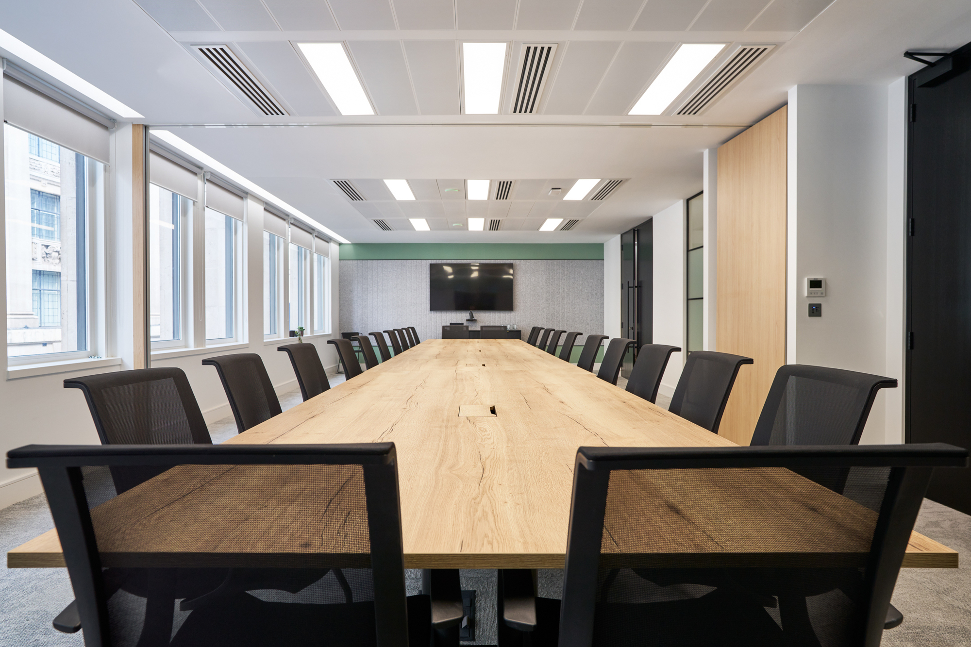 Spacious boardroom in Gemserv’s workspace by Two, featuring a long wooden table, ergonomic chairs, a wall-mounted screen for presentations, and folding walls to divide the meeting room to Gemser’s growing needs.