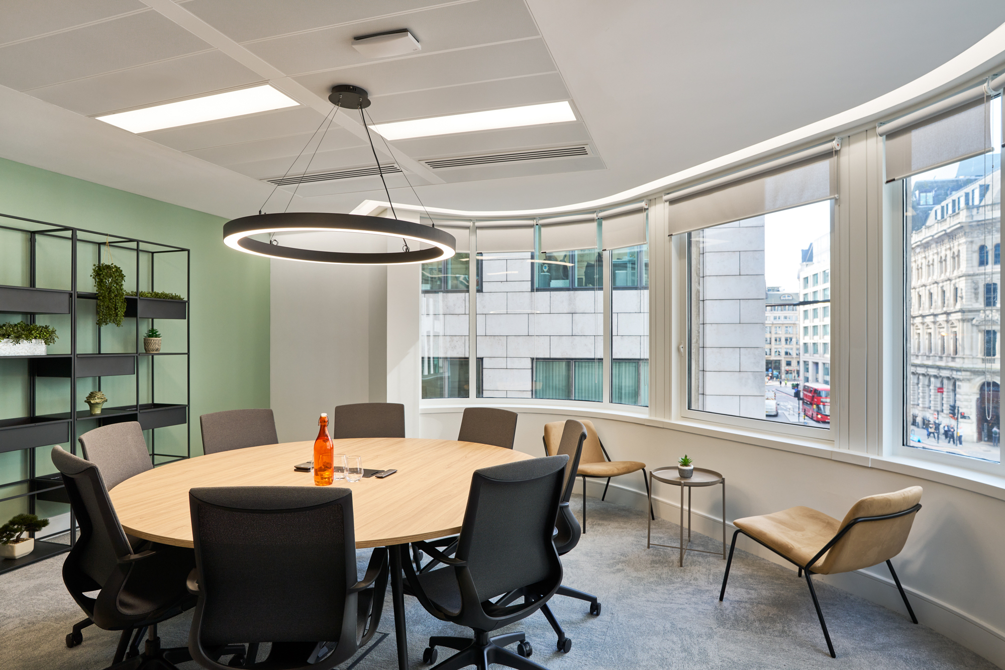 Round meeting room table at Gemserv’s workspace by Two, complemented by ergonomic chairs, floor-to-ceiling windows, and a modern circular light fixture.