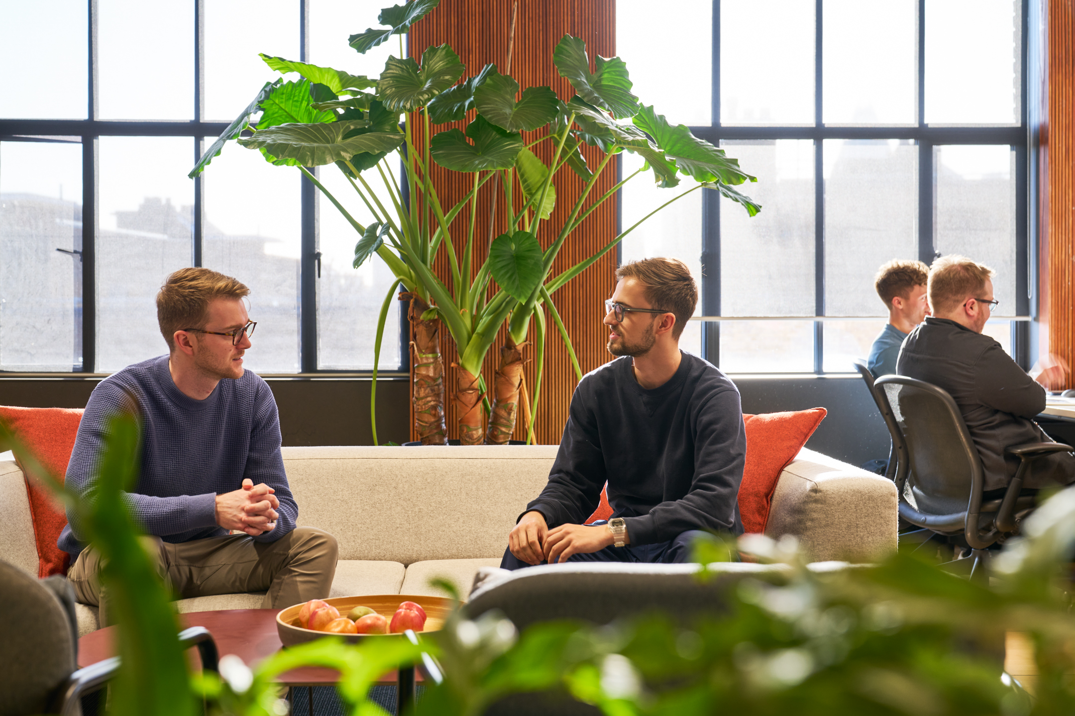 Employees chatting in a relaxed seating area designed by Two, featuring lush greenery and comfortable furniture.