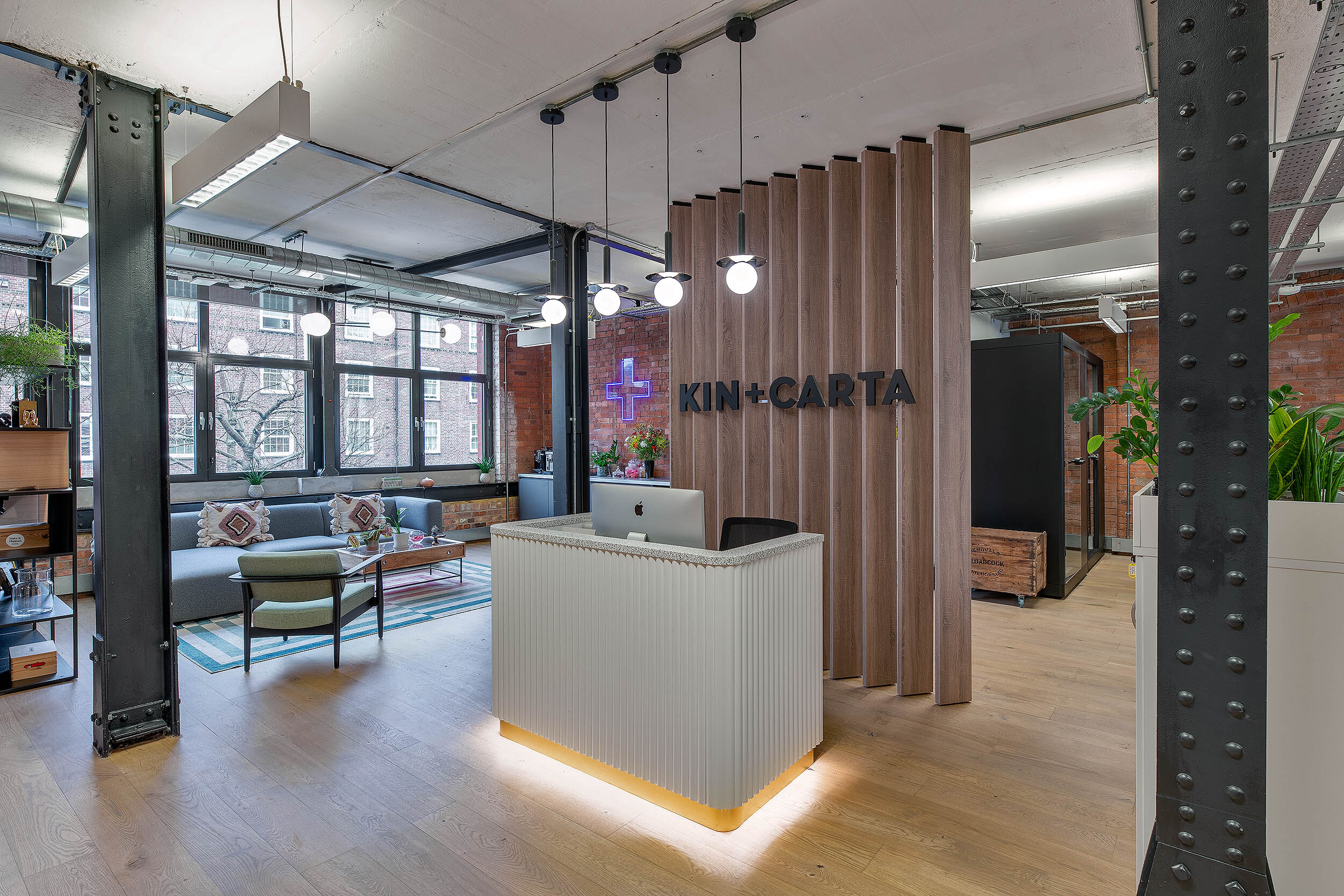 Reception area at Kin & Carta designed by Two, featuring a wood-panelled backdrop, modern desk, and a comfortable lounge space in the background.