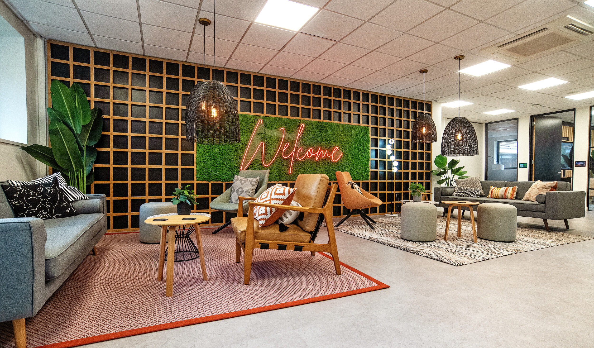 Welcoming lounge area in the Koin office, designed by Two, featuring comfortable seating, greenery, and a bold neon 'Welcome' sign on a moss wall.