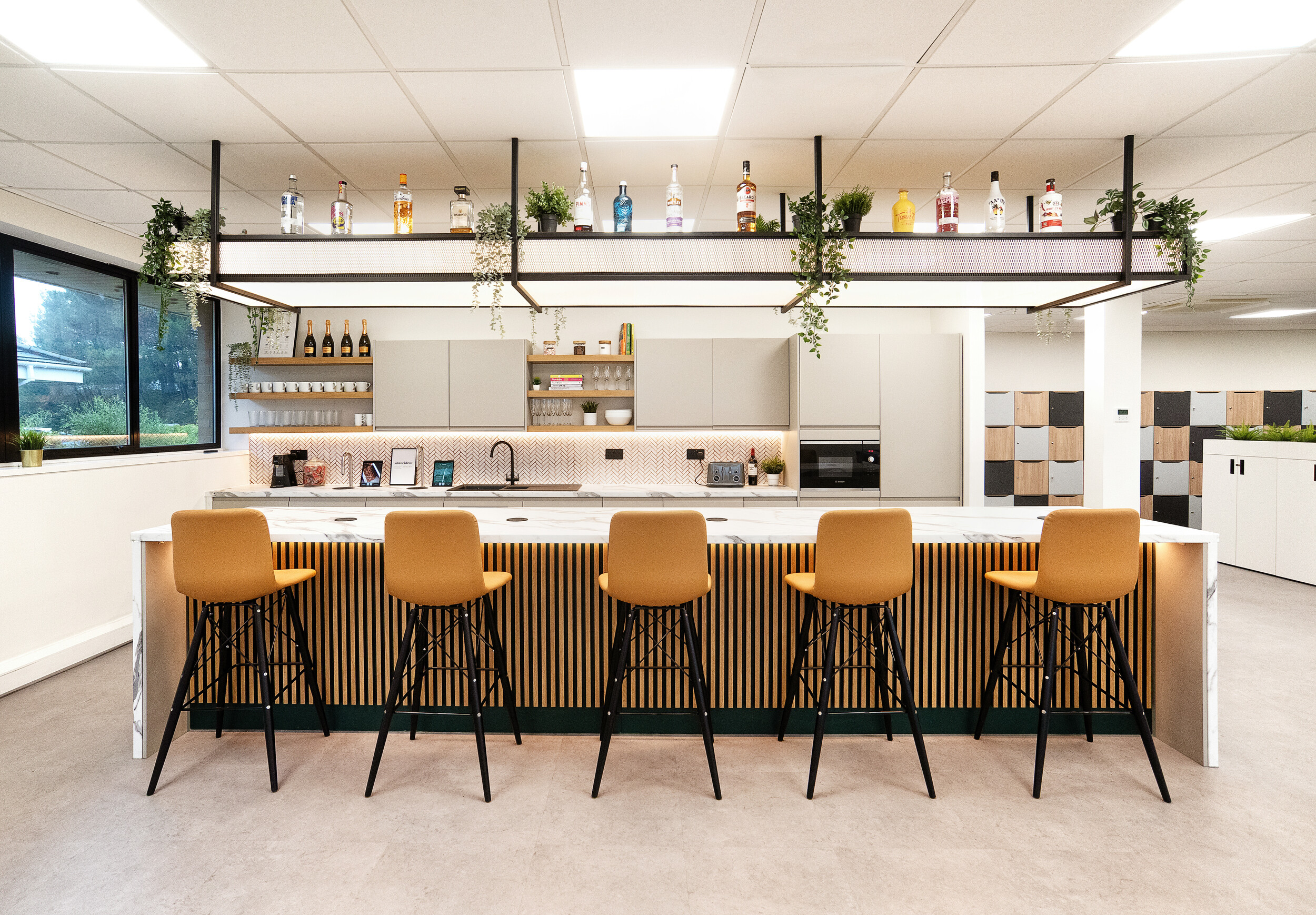 Stylish bar area in the Koin office with a marble countertop, hanging plants, and modern yellow bar stools for a collaborative atmosphere.