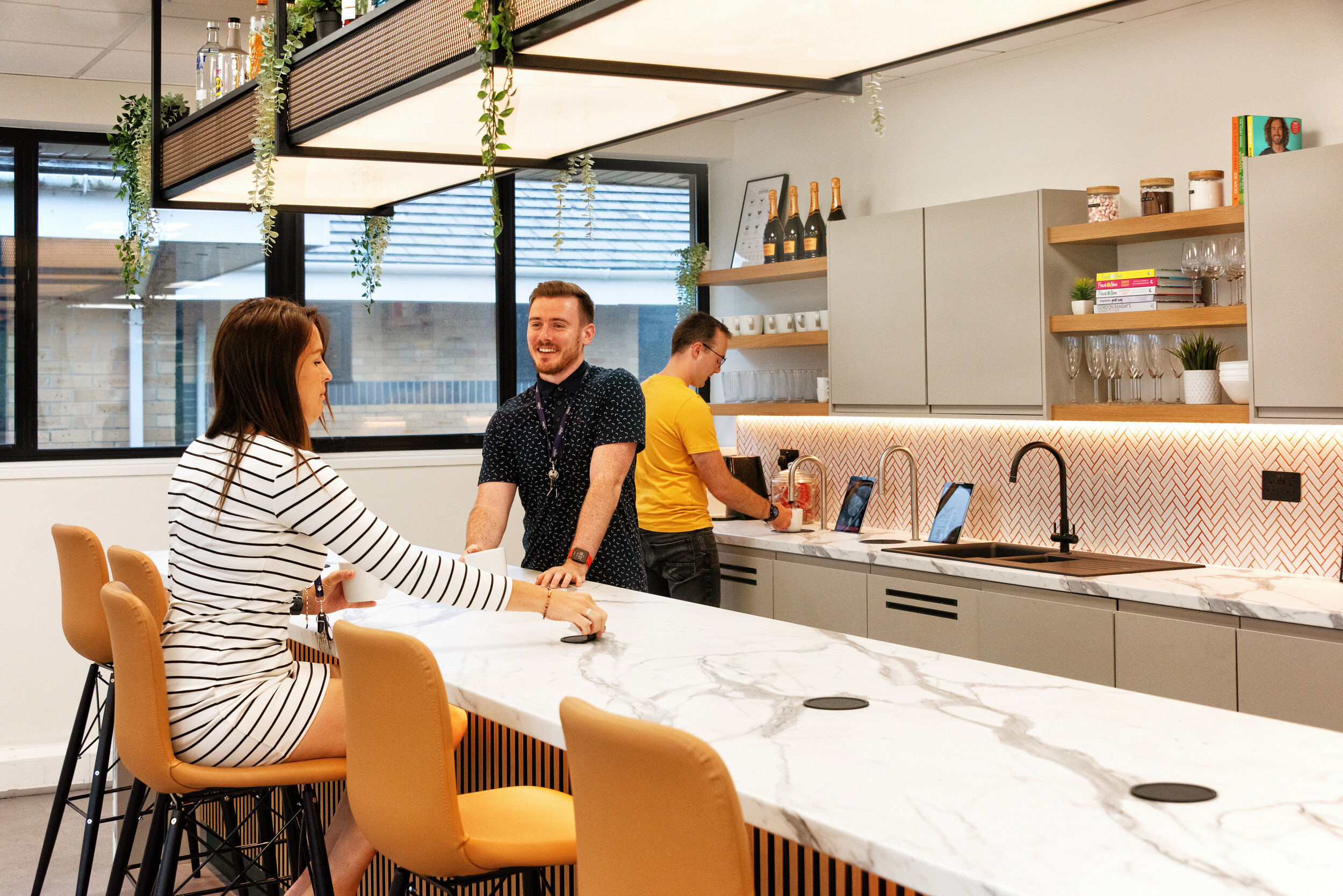 Employees enjoying a coffee break in the Koin office bar area, designed by Two, featuring a functional yet elegant setup with storage and statement lighting.