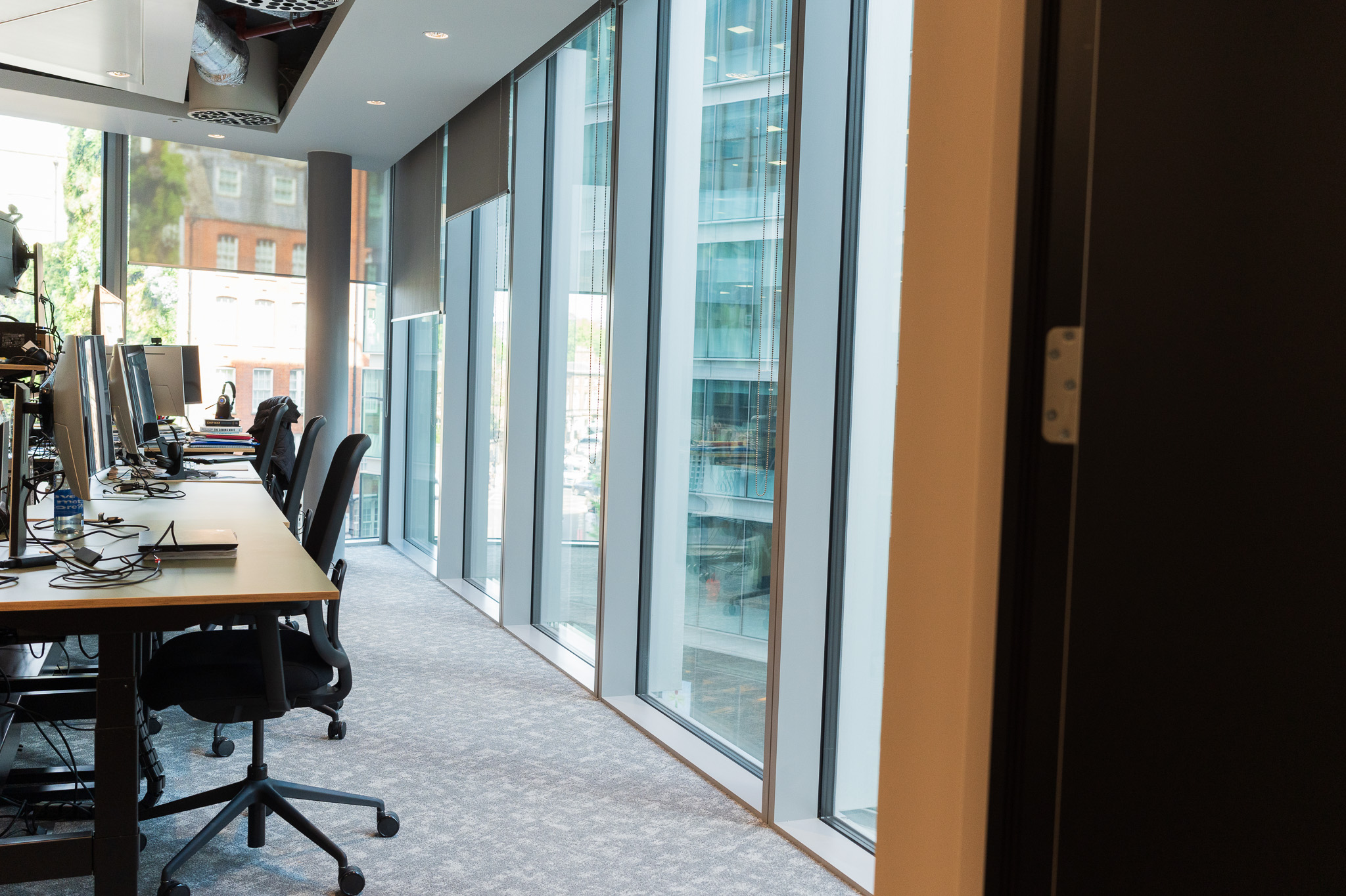 Modern office workspace at Landsec Nova North designed by Two, showing a line of desks beside floor-to-ceiling windows.