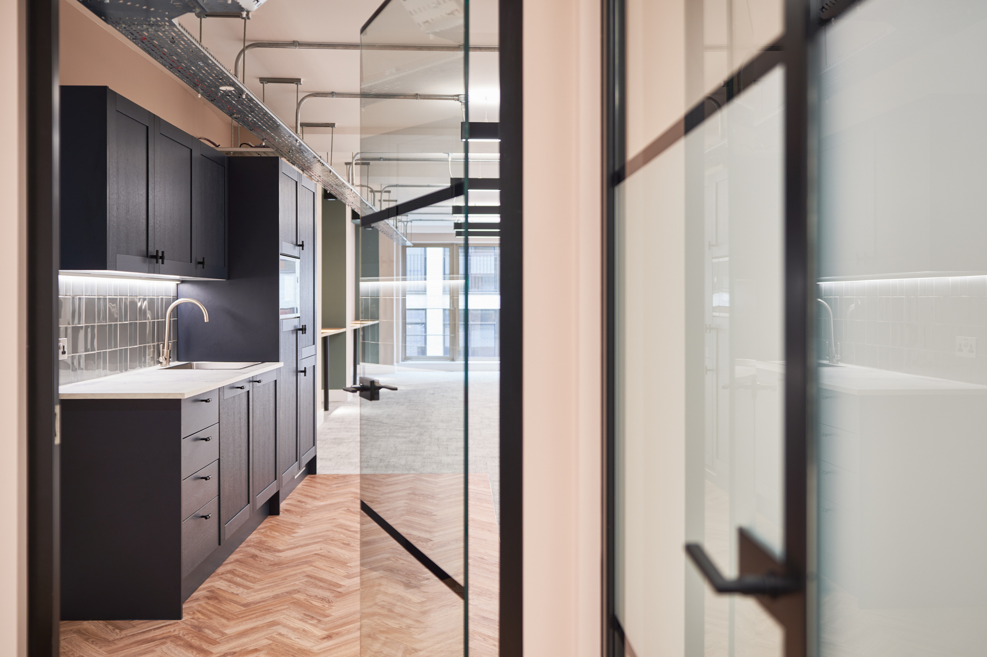 View of a kitchen with dark cabinetry through glass partitioning for Nolan Partners.