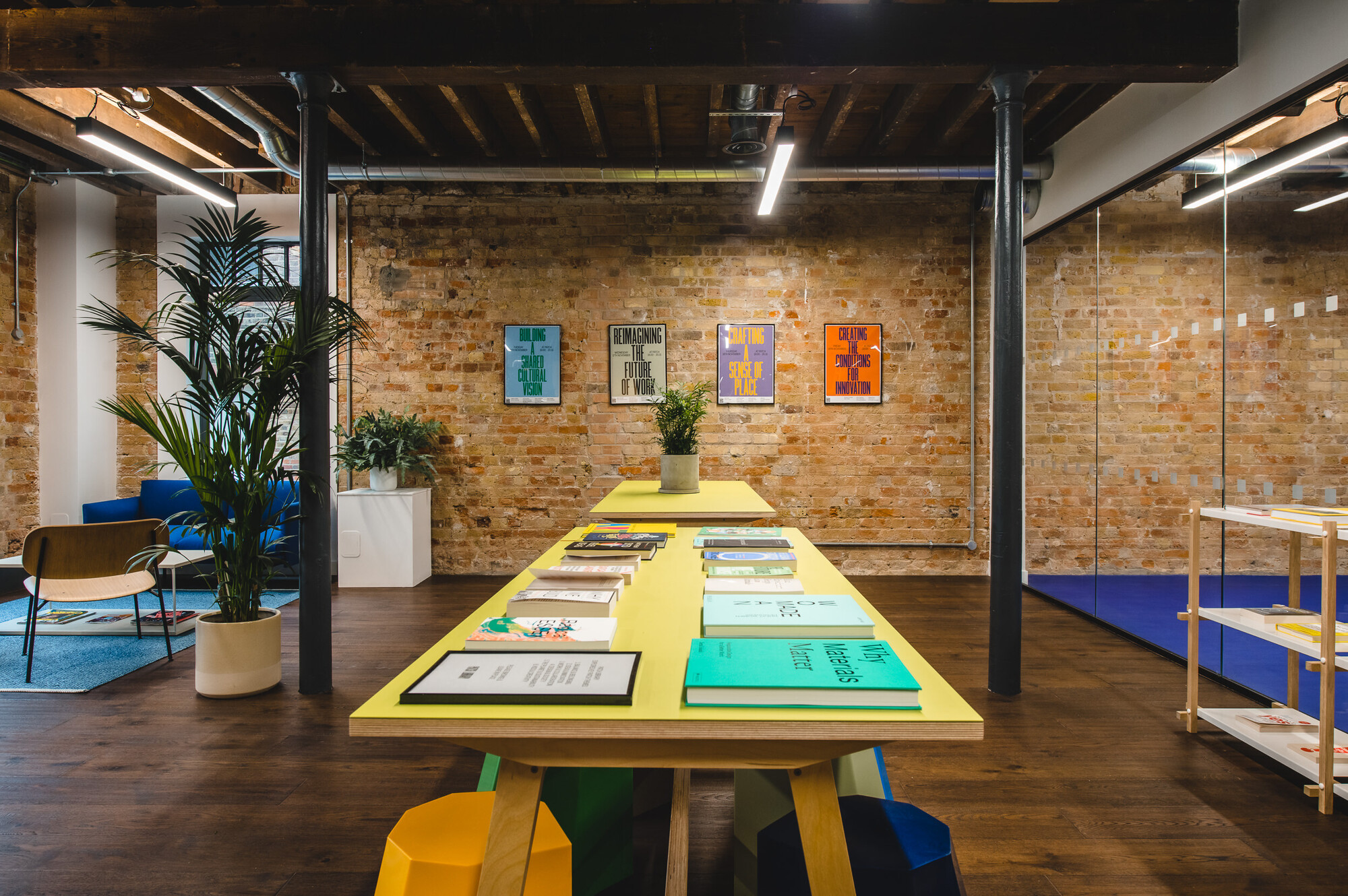 Creative co-working space at Patch by Two, featuring a central display table with books, exposed brick walls, and a mix of vibrant seating areas.