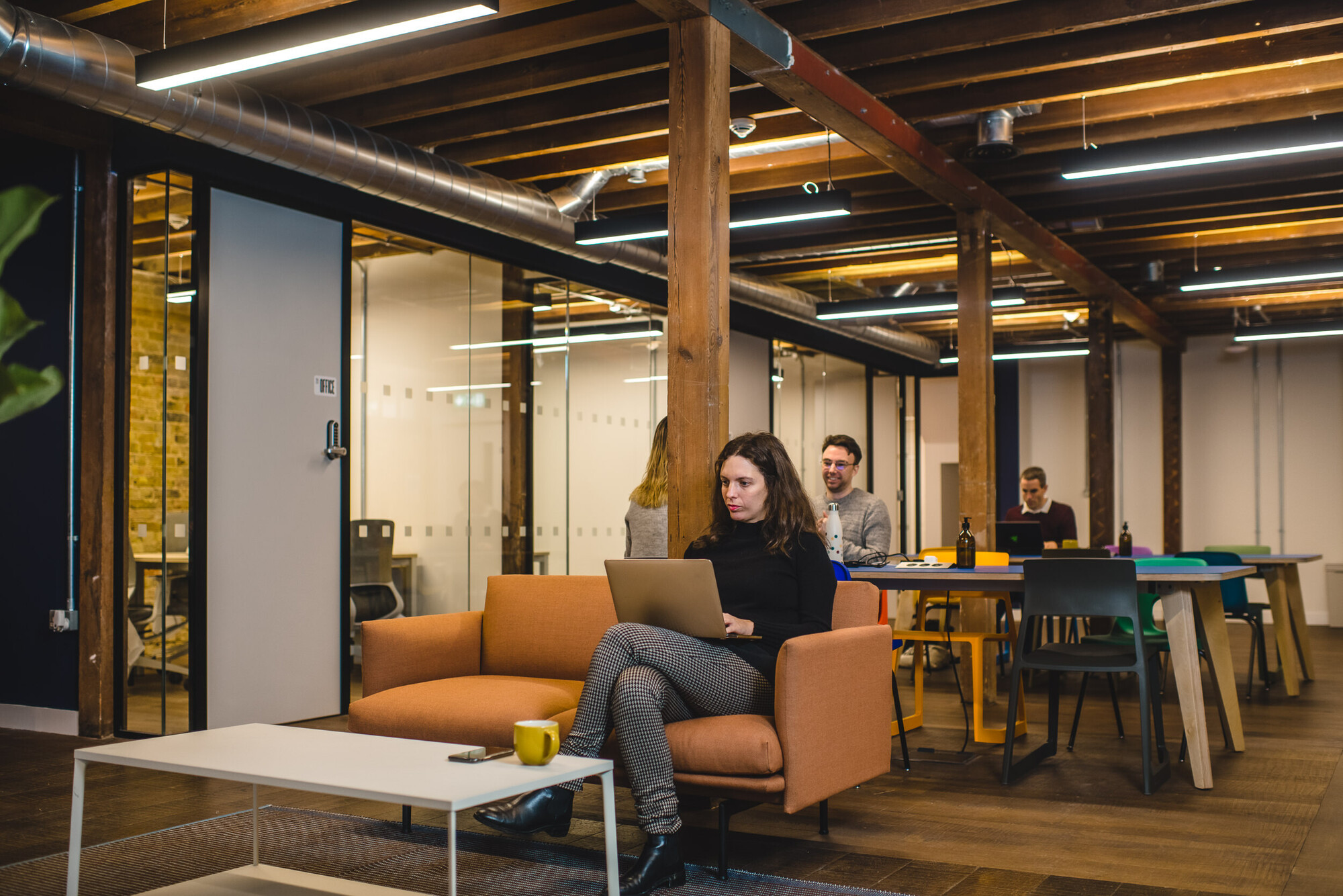 Collaborative workspace at Patch by Two, featuring long shared desks, ergonomic chairs, and greenery against exposed brick walls.