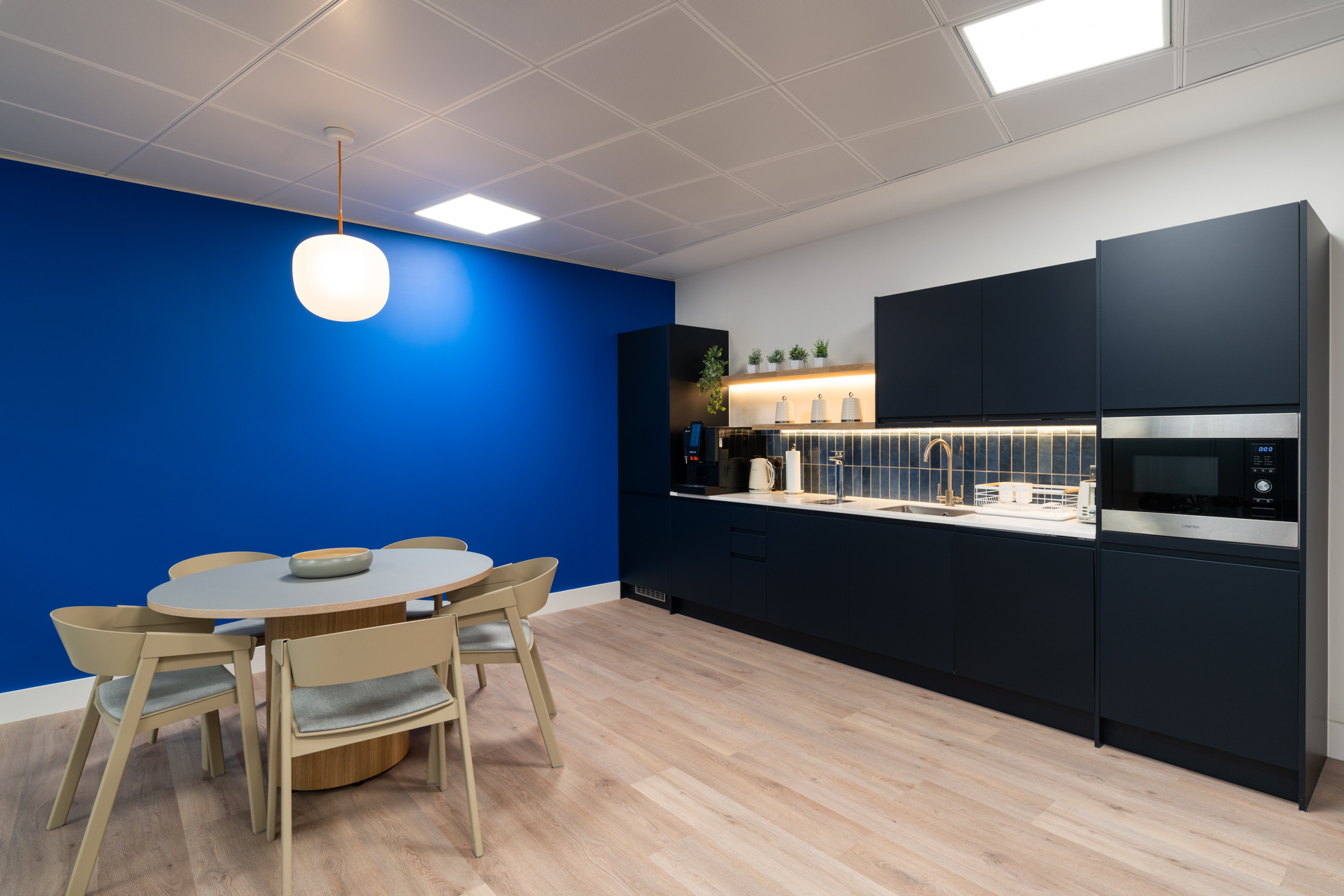 Teapoint area at the Port of London Authority office designed by Two, featuring a bold blue accent wall, light wood flooring, and a modern dining setup.