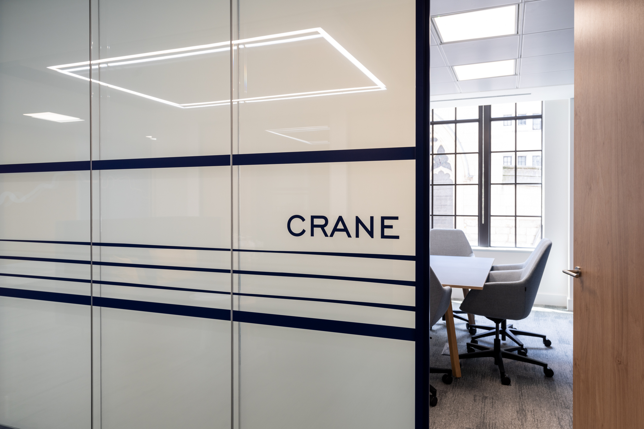 Crane meeting room at the Port of London Authority office by Two, featuring frosted glazing with navy accents and a view of the workspace.