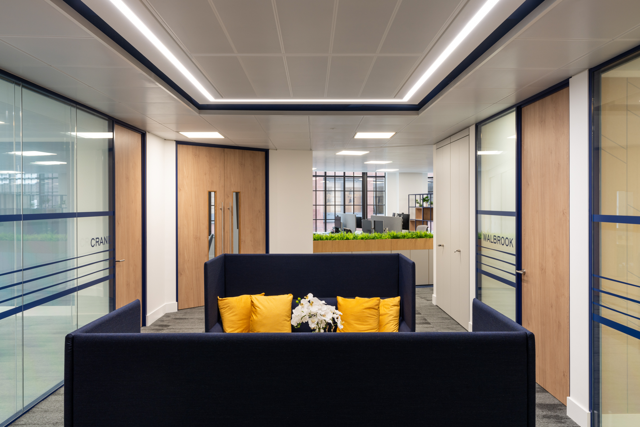 Hallway in the Port of London Authority office by Two, with navy high-back seating, yellow accents, and glass meeting rooms named Crane and Walbrook.