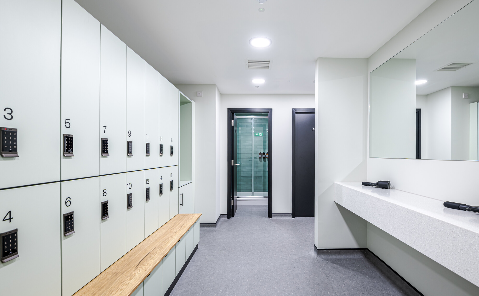 Modern locker room at ReFIT Gym, 100 Wood Street, with numbered lockers, a wooden bench, and vanity mirrors.