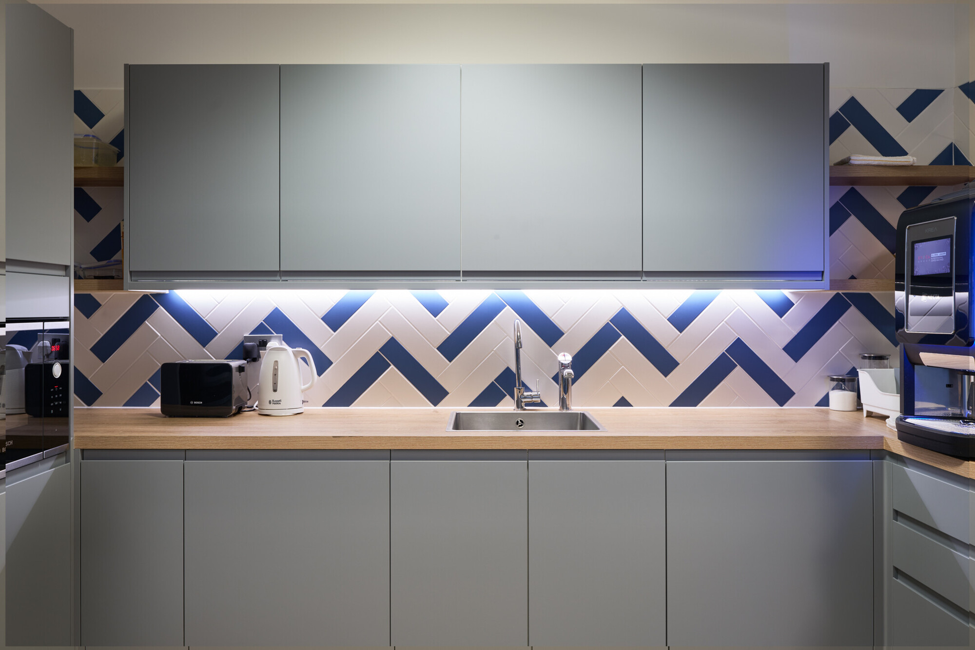 Teapoint at Tech UK fitted out with blue and white tile design, grey overhead cabinets and overhead lighting