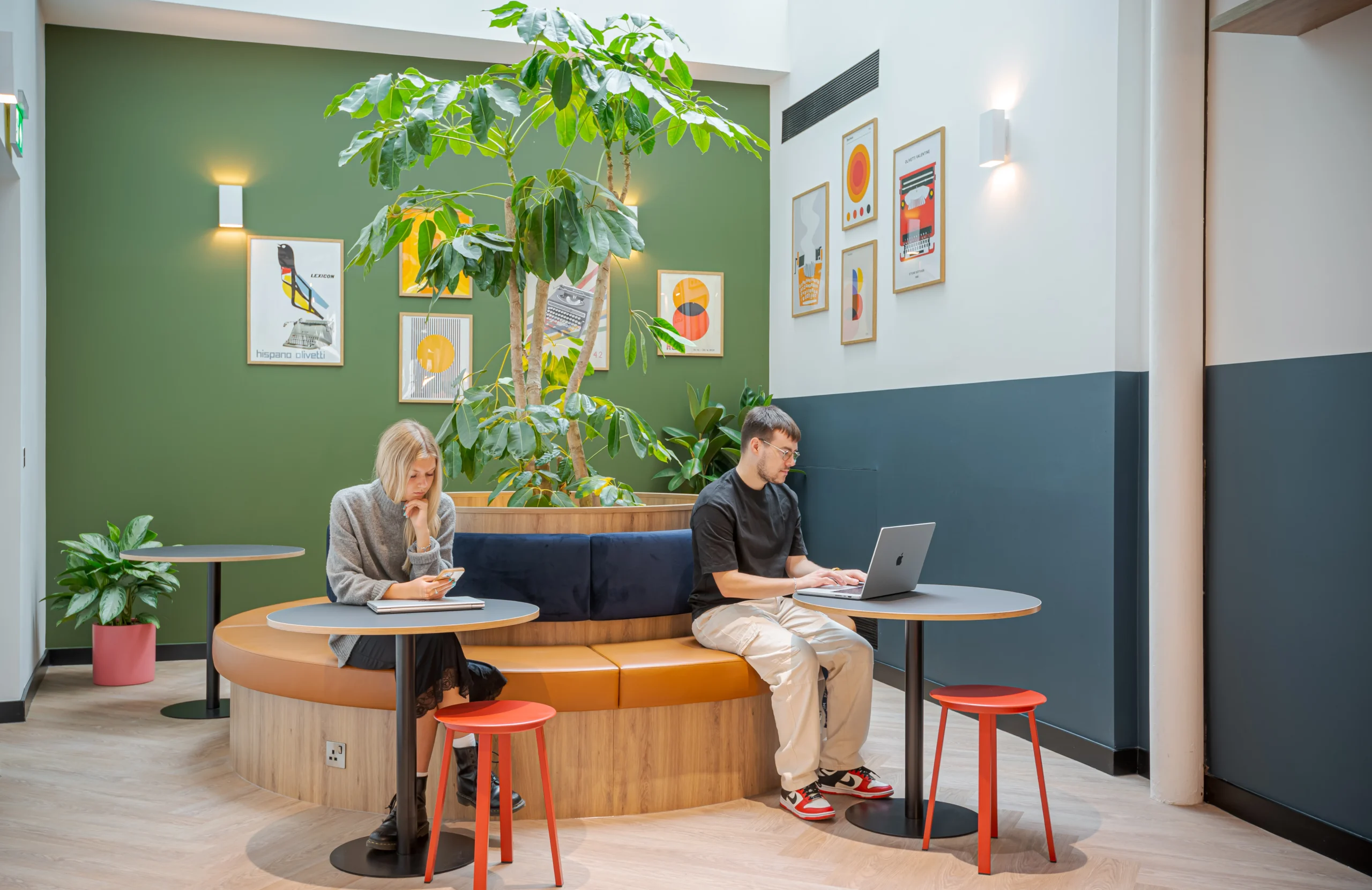 Work.Life at the Typewriter Building designed by Two, with a winter garden that includes a circular wooden bench, lush indoor plants, vibrant artwork, and modern tables with colourful stools.