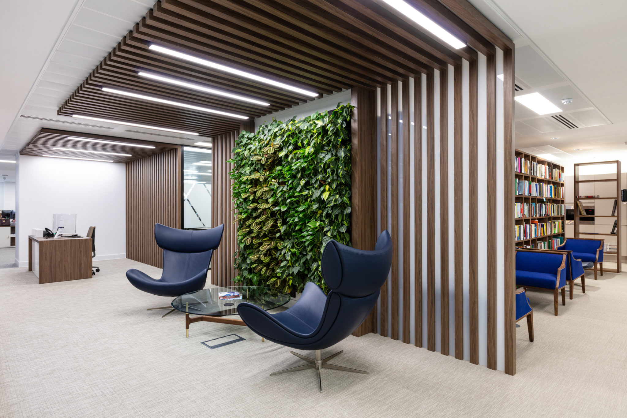 Elegant lounge area in an Urban Exposure workspace designed by Two, featuring a green living wall, modern wood paneling, and stylish navy seating.