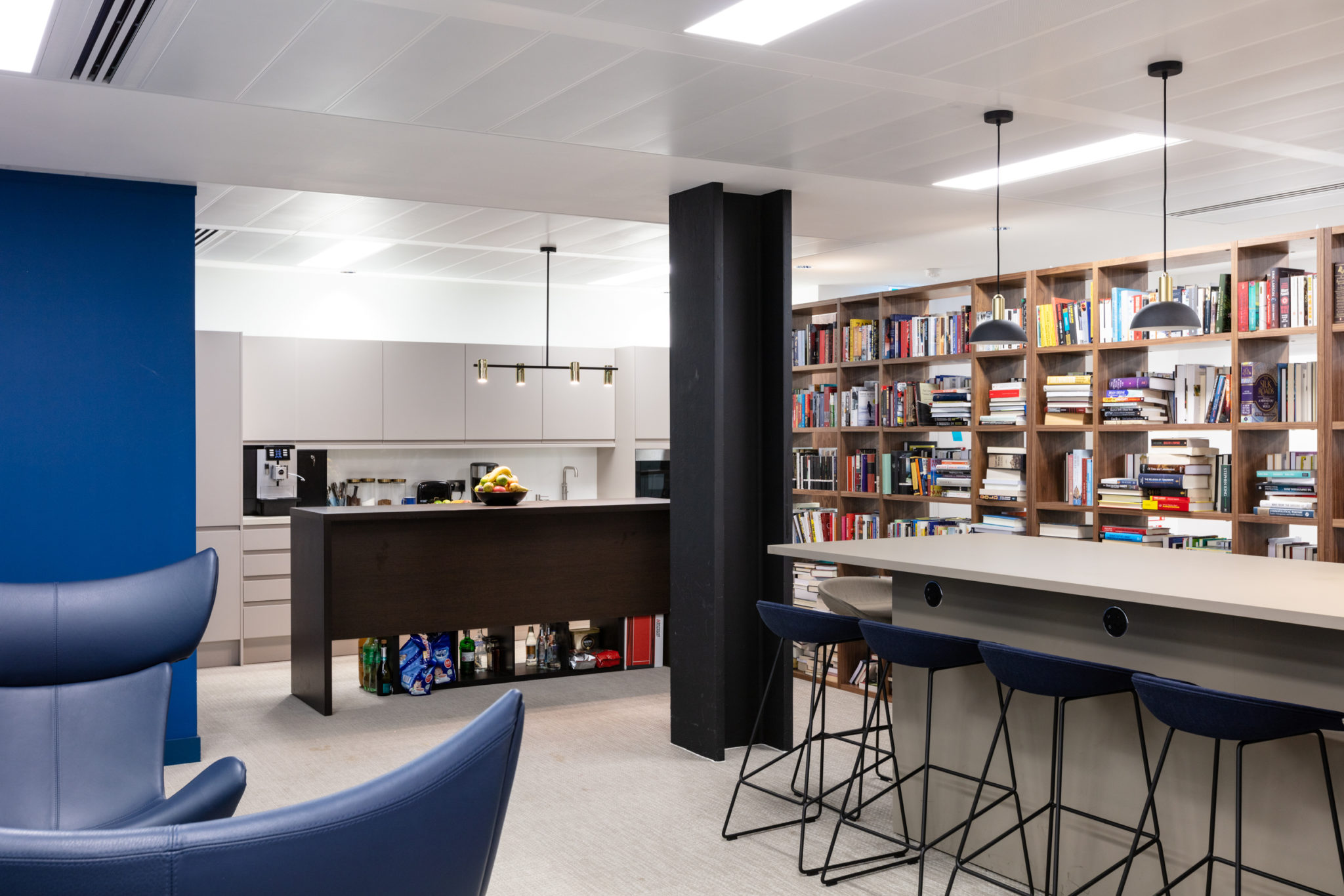 Inviting library area in the Urban Exposure workspace by Two, with floor-to-ceiling bookshelves, a communal bar-style table, and pendant lighting for a sophisticated atmosphere.