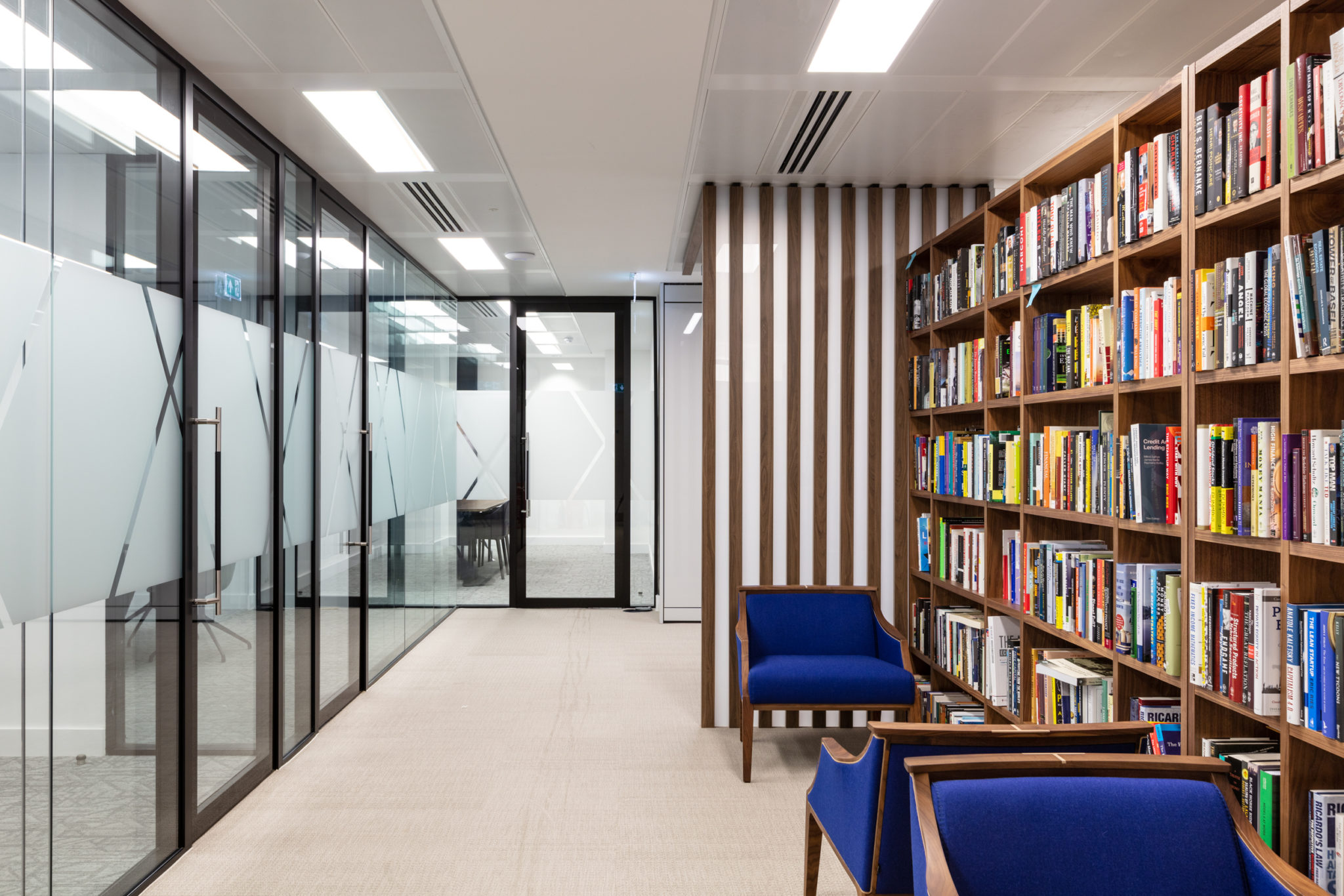 Library-inspired workspace at Urban Exposure by Two, complete with built-in bookshelves, vibrant blue seating, and glass-walled meeting rooms for a dynamic office layout.