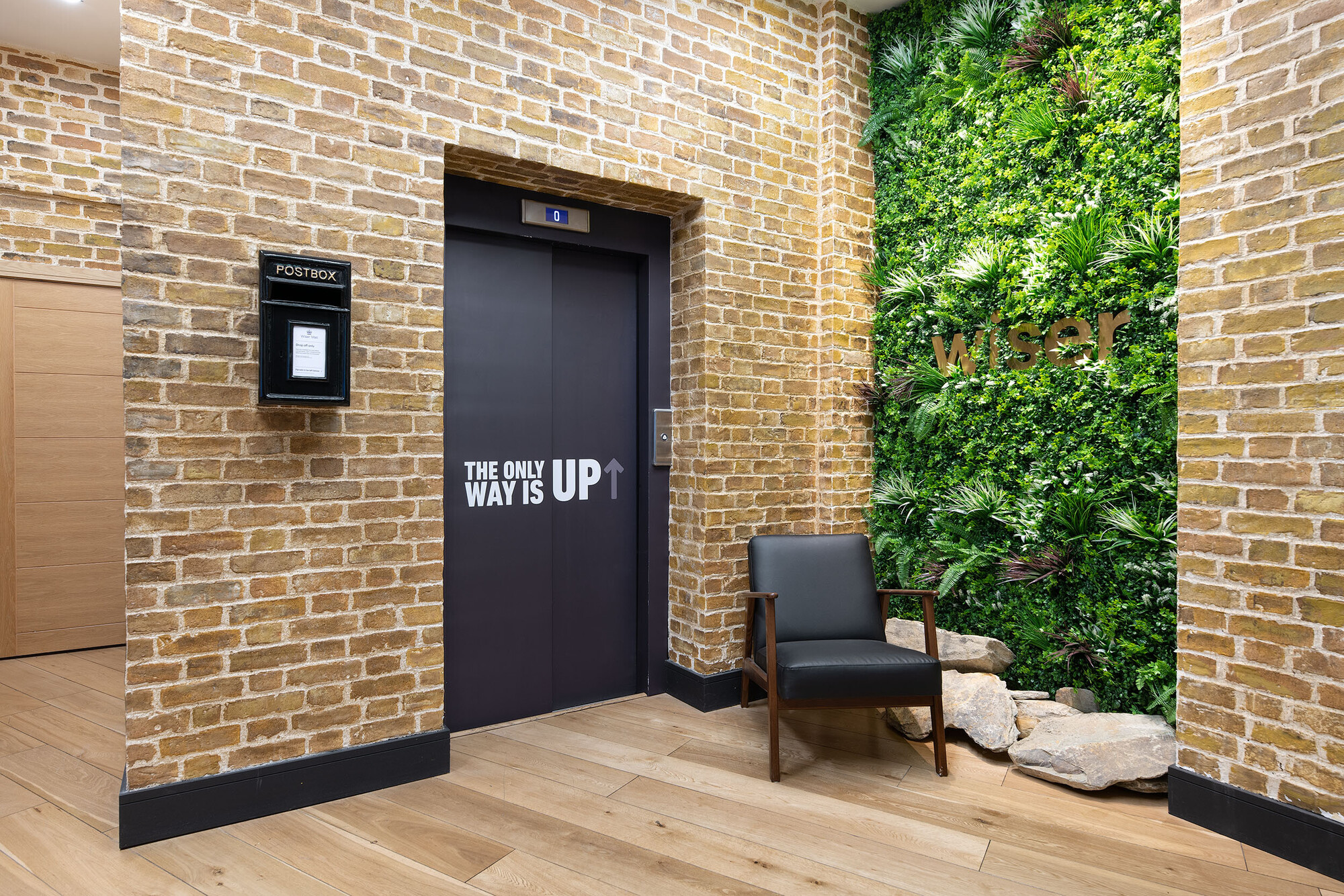 The Wiser office entrance by Two, featuring a green wall with the company name and exposed brick accents, blending natural and industrial elements.