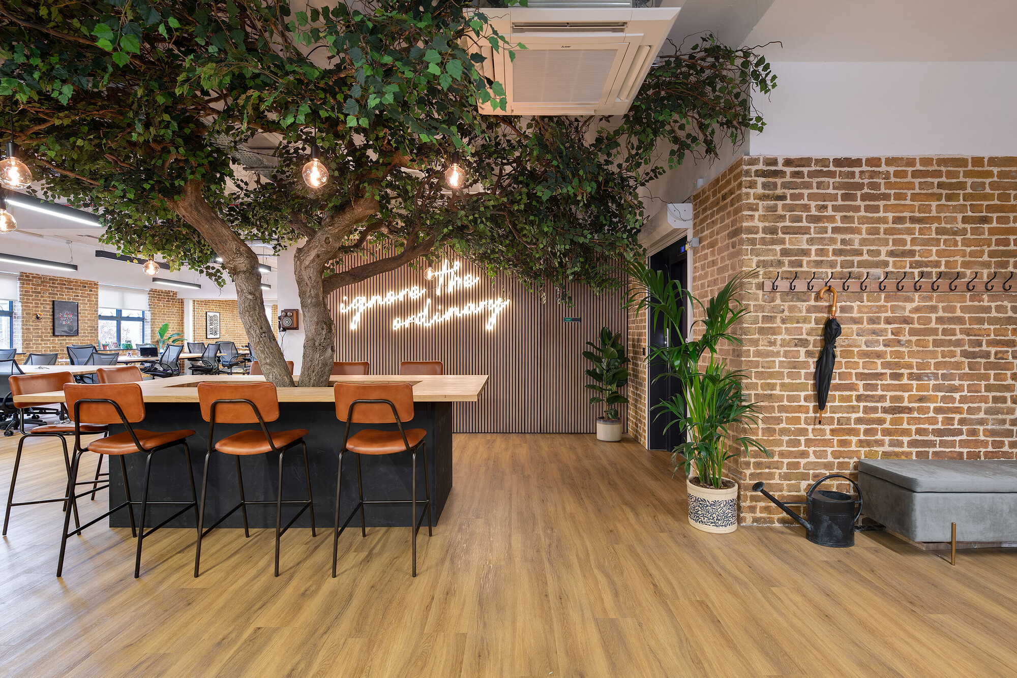 Workspace at Wiser designed by Two, featuring a tree-centred table with leather bar stools and exposed brick walls for a natural, creative vibe.