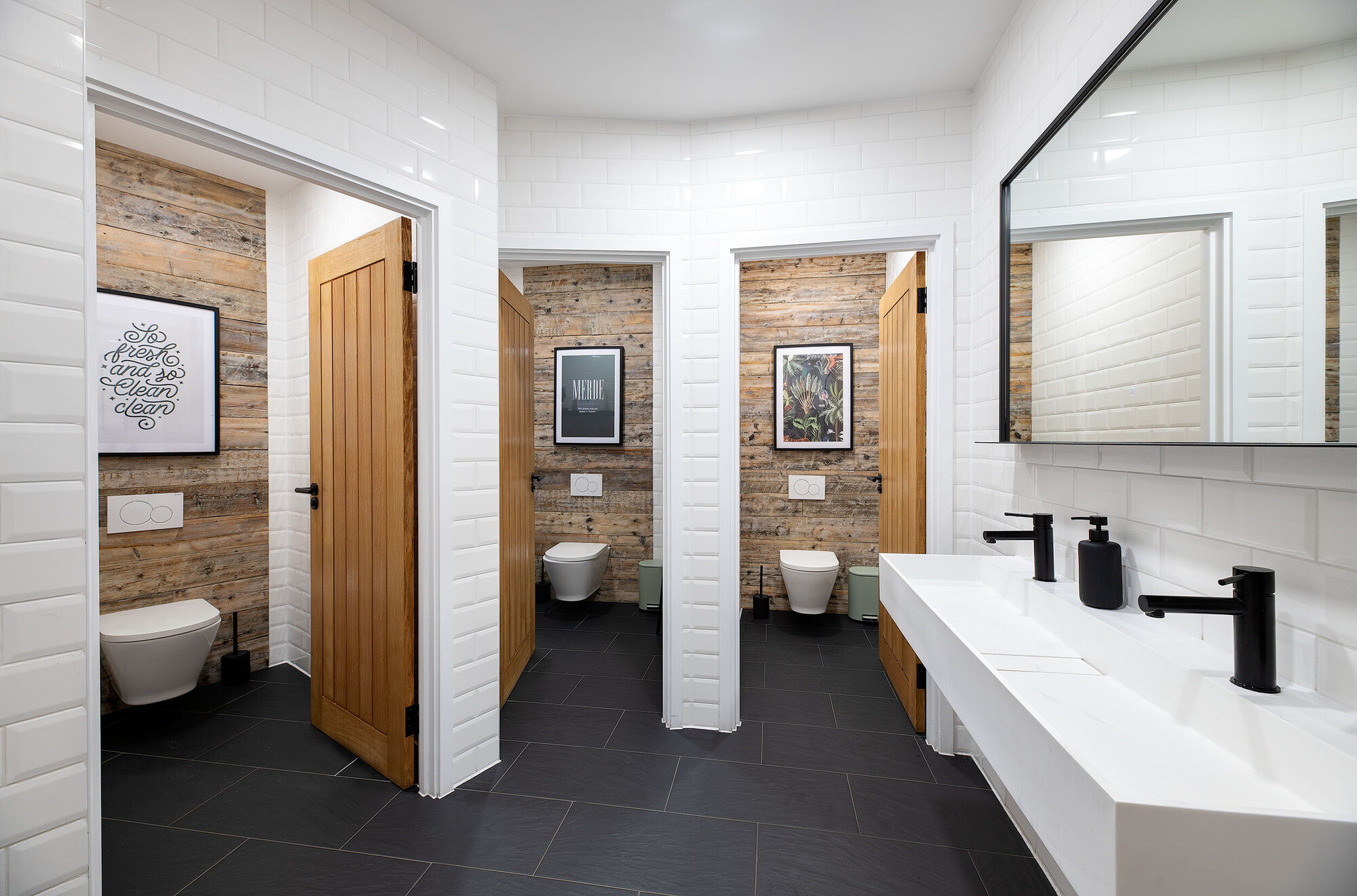 Industrial-inspired restroom design with rustic wooden panelling and modern white tiling at Wiser's office by Two.