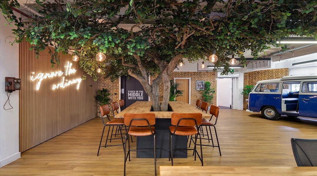 Central workspace at Wiser with a custom-built collaboration table surrounded by greenery and a vintage VW camper van, designed by Two.