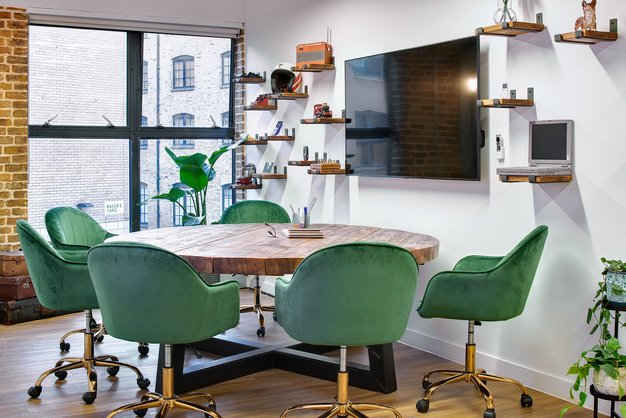 A close-up of the Ideation Station in Wiser’s office, designed by Two, with green velvet chairs and a rustic wooden table surrounded by decorative shelving.