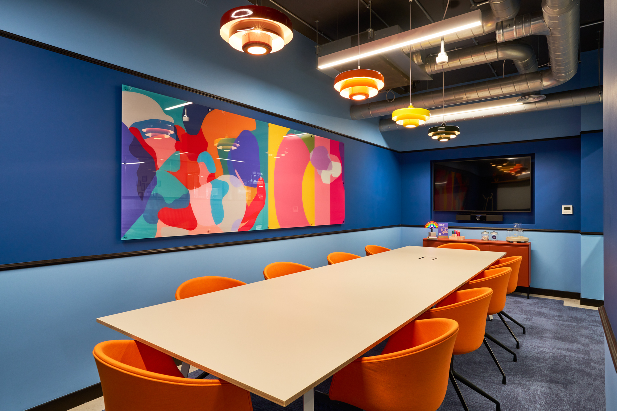 The vibrant meeting room “Pride” at Work.Life Waverly House by Two, featuring bold blue walls, orange chairs, and colourful artwork inspired by Soho's energy.