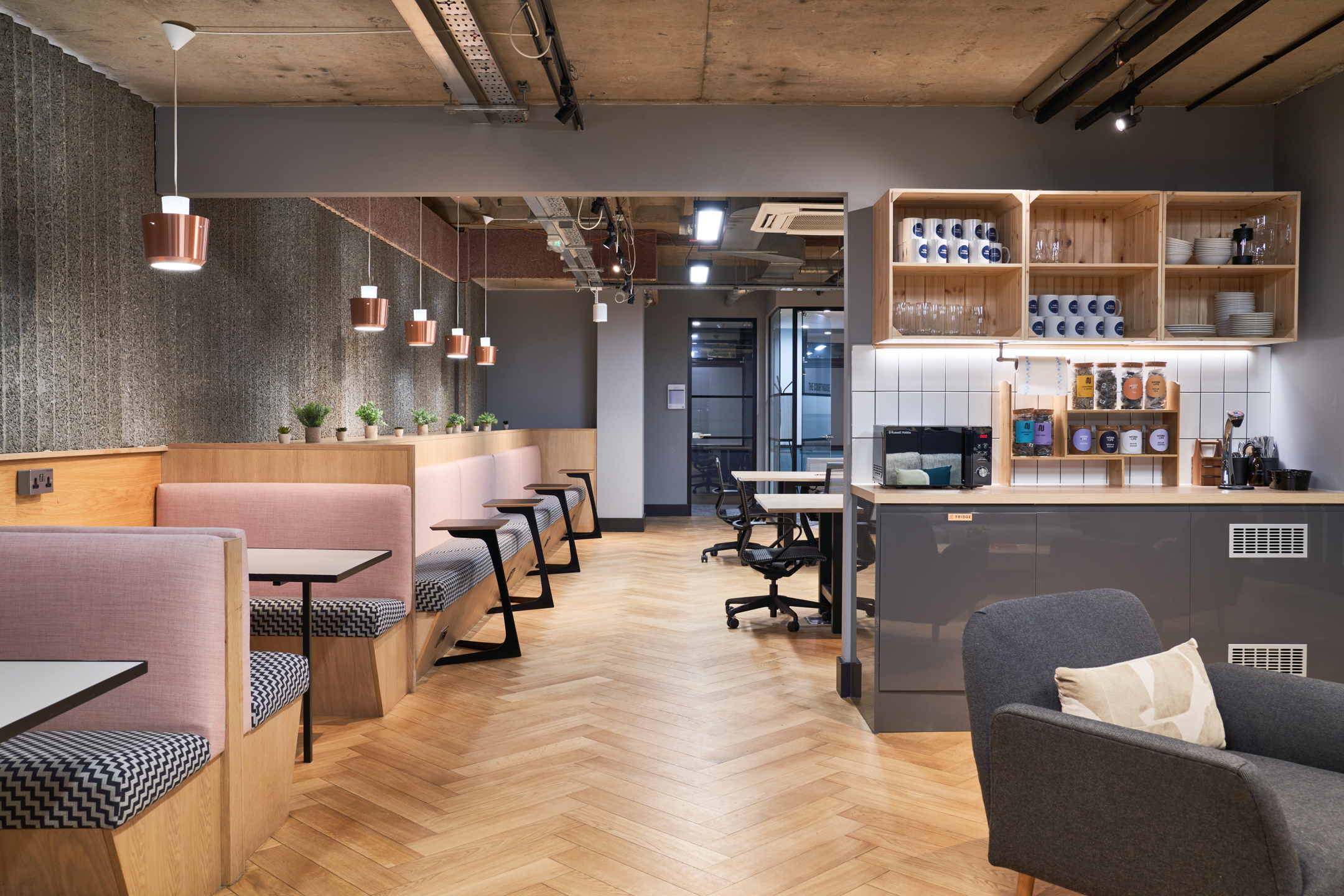 A stylish workspace at Work.life Liverpool Street designed by Two, featuring cosy booth seating with soft pink tones, modern lighting, and a kitchenette for collaborative work and coffee breaks.