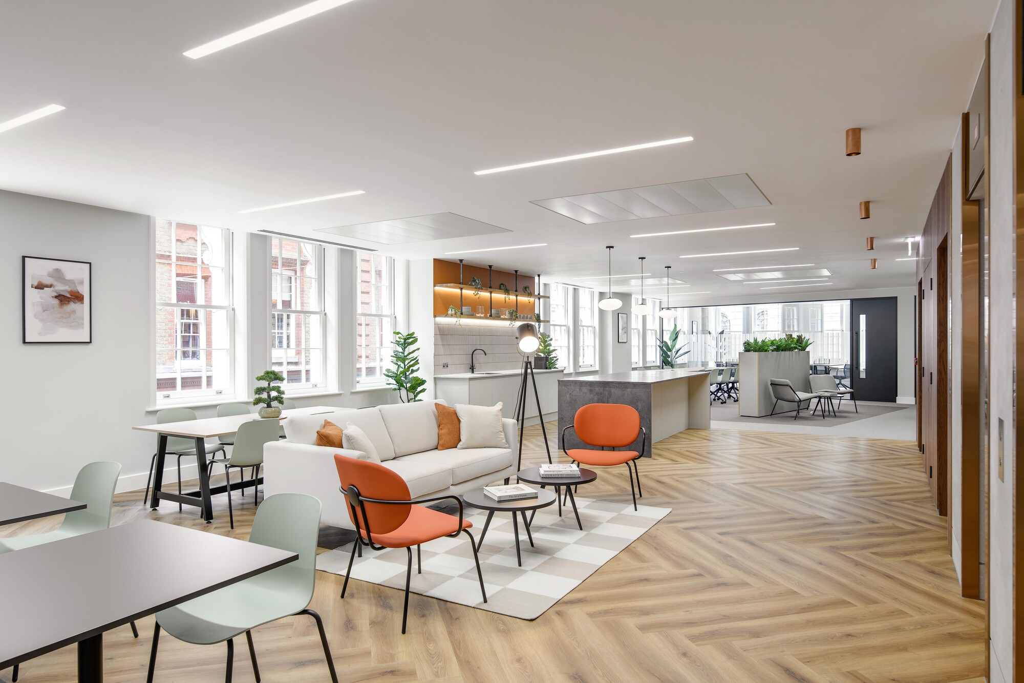 A bright Tenant-Ready™ workspace designed by Two for an Asset Management Firm, featuring herringbone vinyl flooring, vibrant seating, and large bay windows.