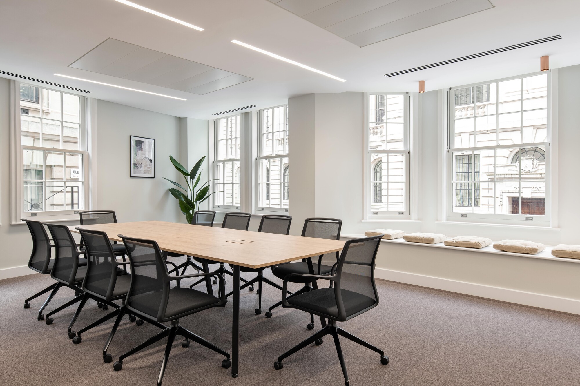 Modern meeting room in the Tenant-Ready™ workspace by Two, featuring ergonomic chairs, a wooden table, and cushioned bay window seating for added versatility.