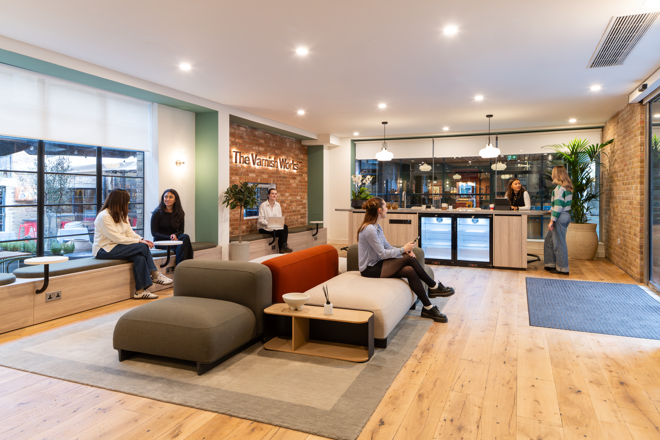 The Varnish Works recepetion area, with bespoke signage, coloured seating with Two employees having a coffee.