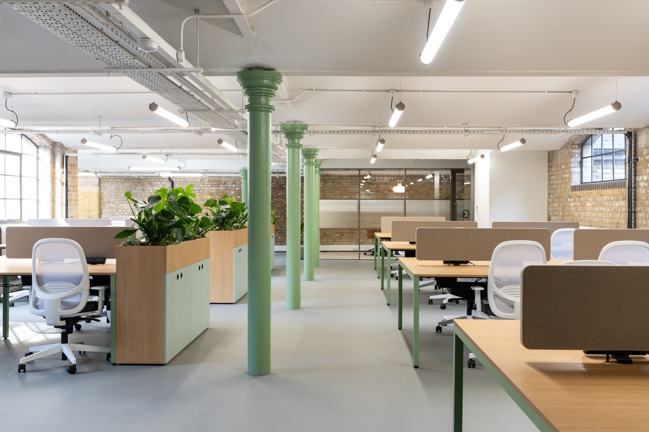 The Varnish Works open workspace, featuing tall sage green beams, plotted biophilic plants and seating area.