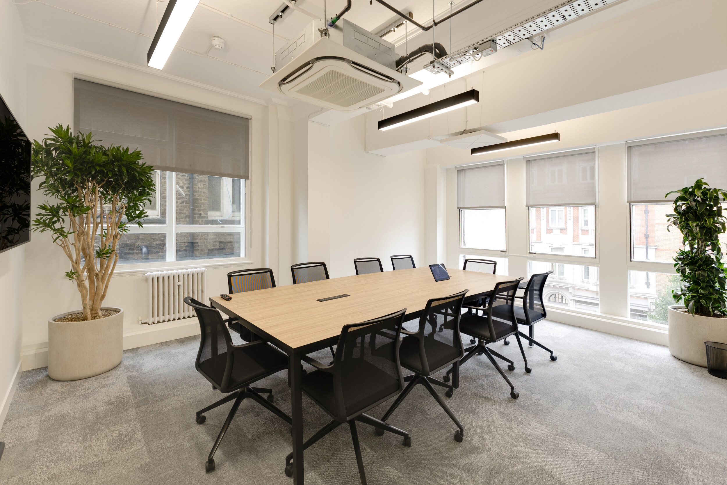 InPost meeting room with large wooden conference table, black mesh chairs, potted plants, and floor-to-ceiling windows with grey blinds.