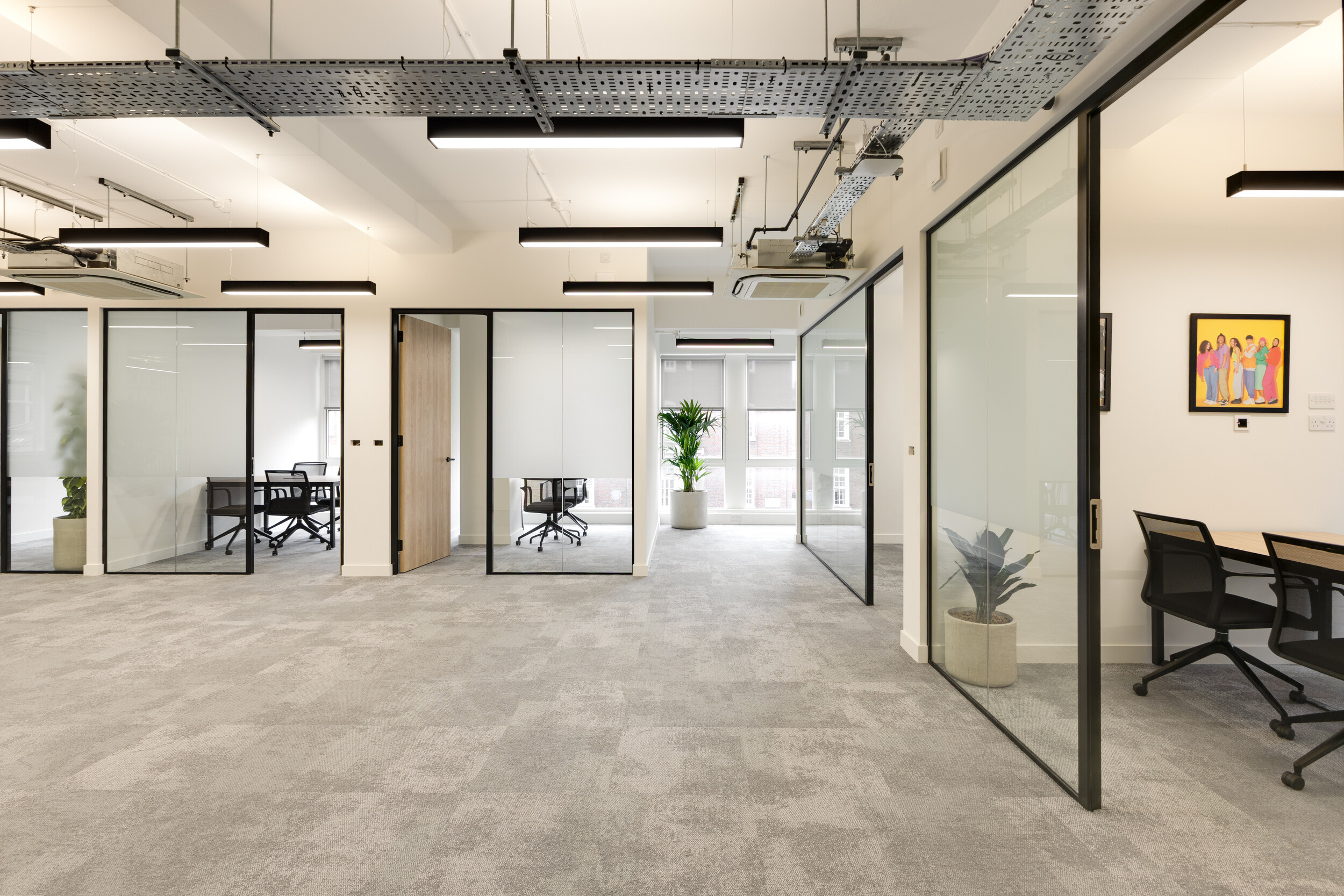 InPost open-plan office with glass-partitioned meeting rooms, grey carpet, potted plants, and exposed ceiling cable trays with modern lighting.