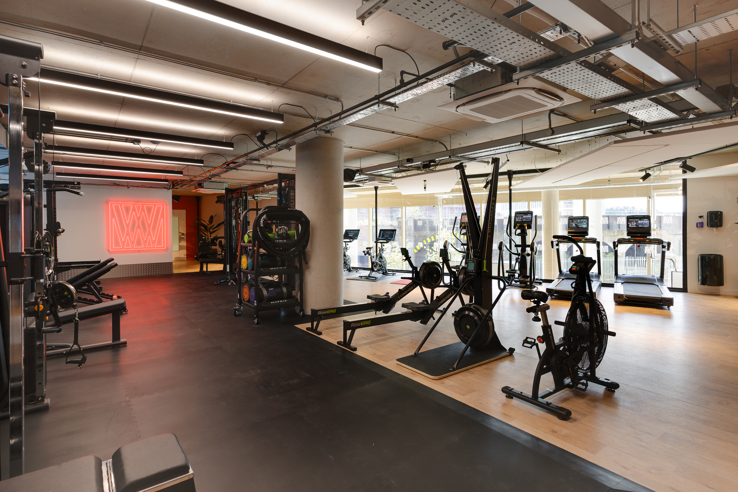 Spacious gym at reFIT Bristol, the Welcome Building, featuring treadmills, bikes, rowing machines, and weightlifting equipment with a red neon ‘W’ logo on the back wall.