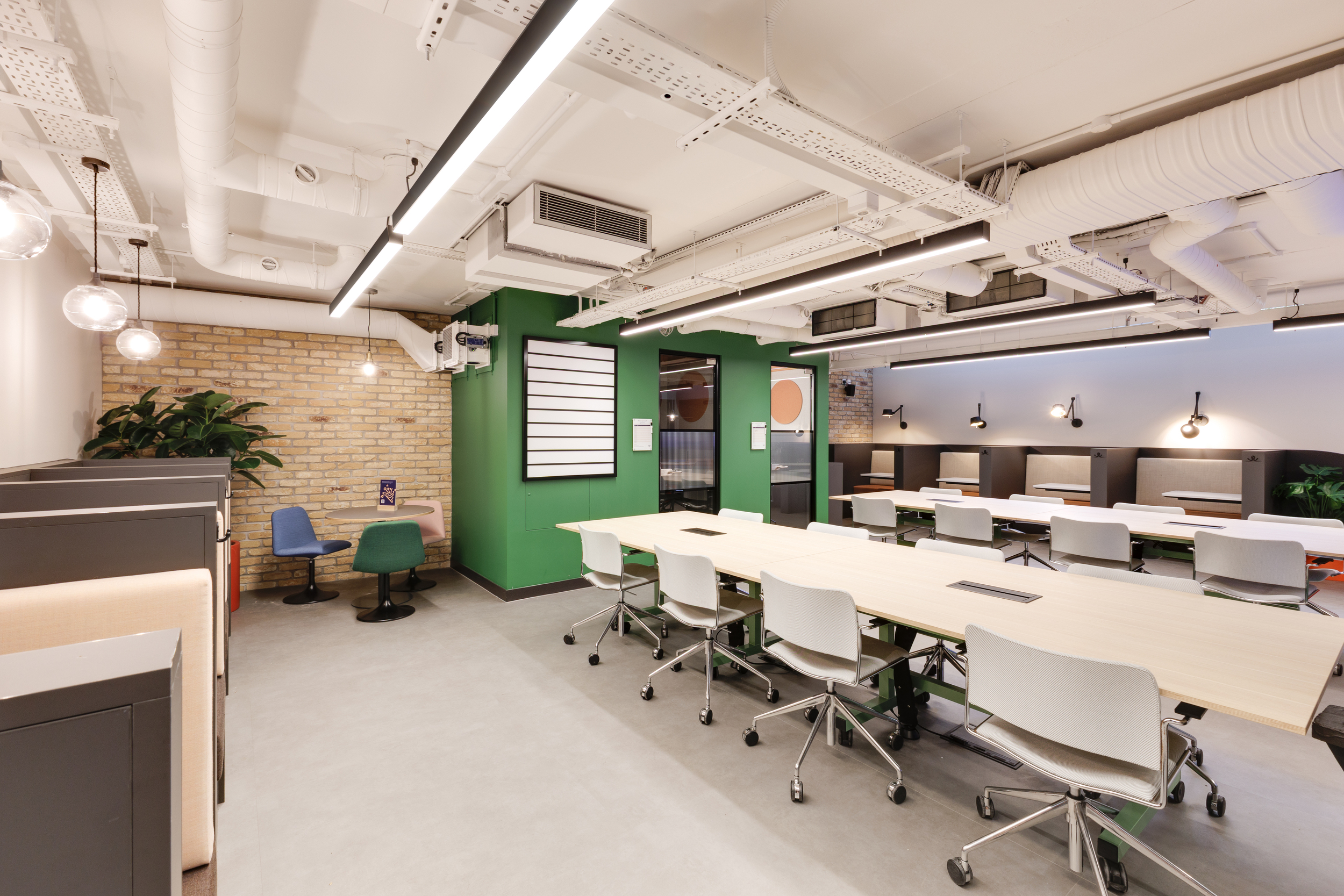 Open coworking area at Work.Life Clerkenwell Green with green walls, shared desks, and booth seating, completed by Two.