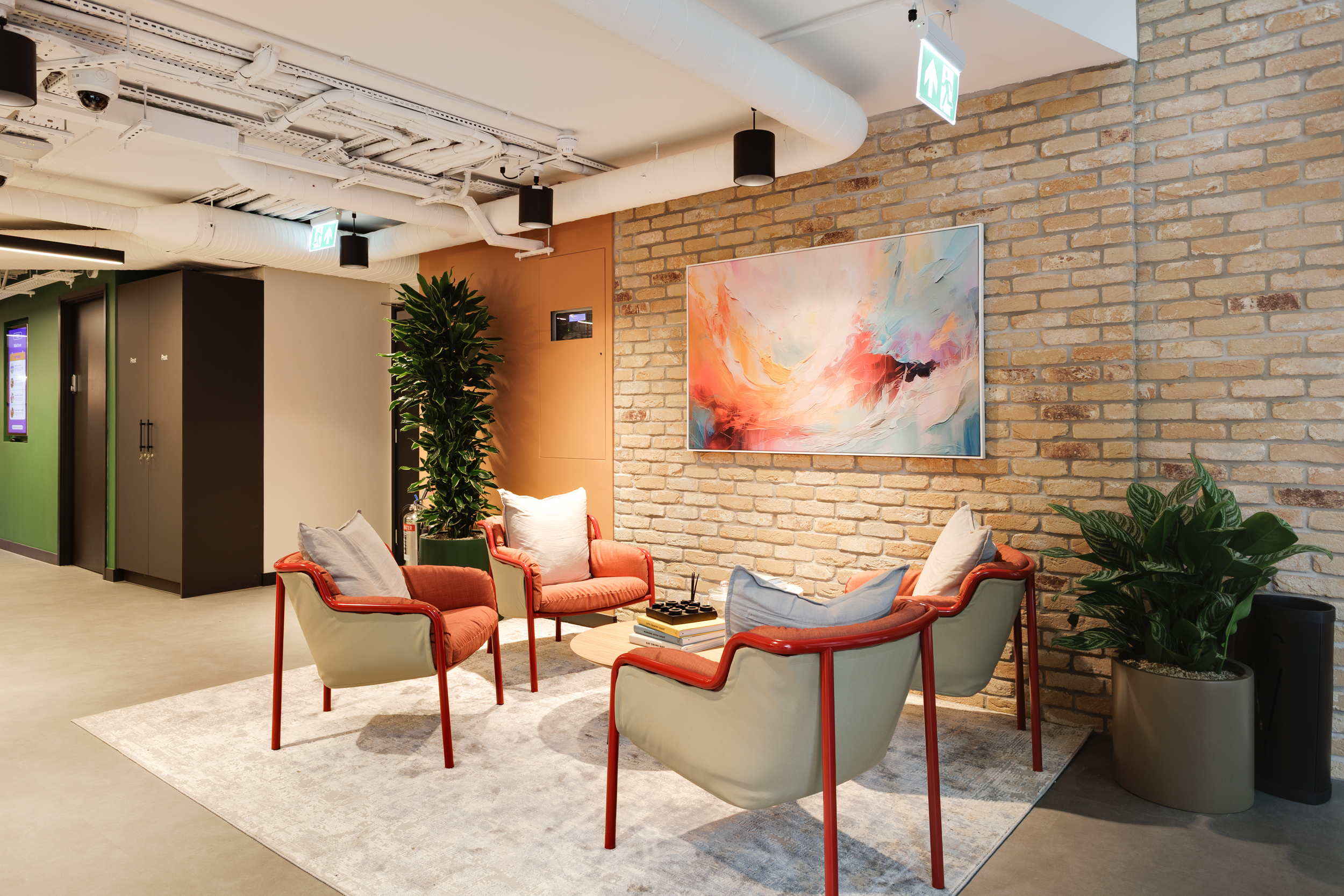 Lounge area at Work.Life Clerkenwell Green with brick walls, colourful artwork and red-framed armchairs, completed by Two.